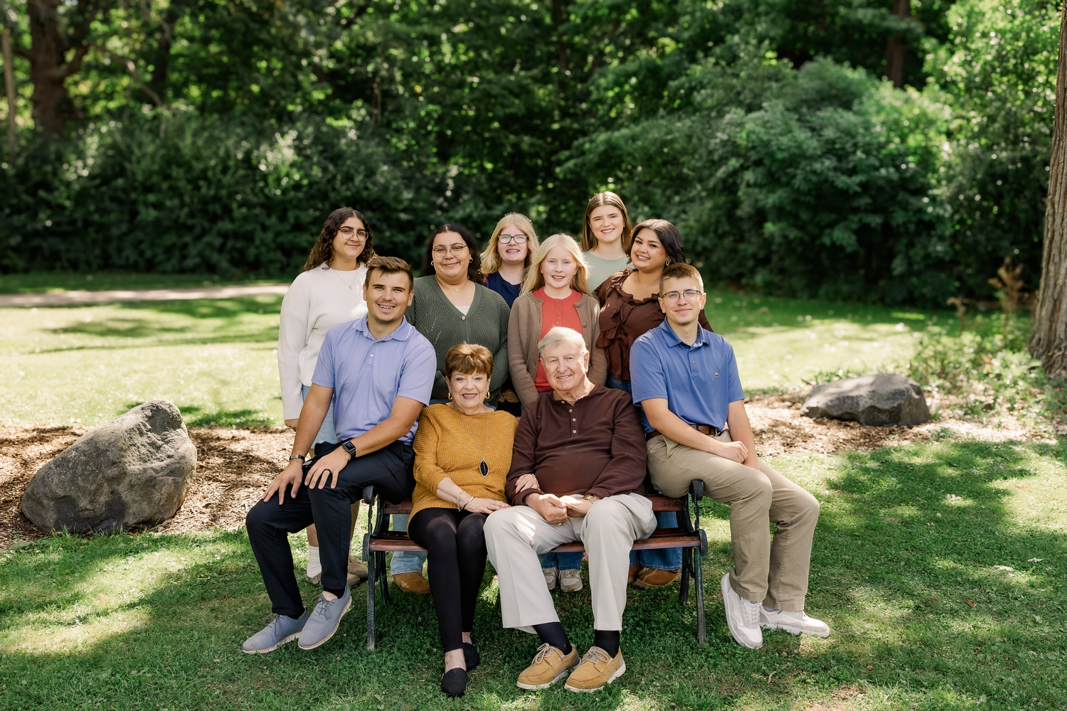 Large family in a grassy field standing and sitting close together smiling surrounded by vibrant fall foliage.