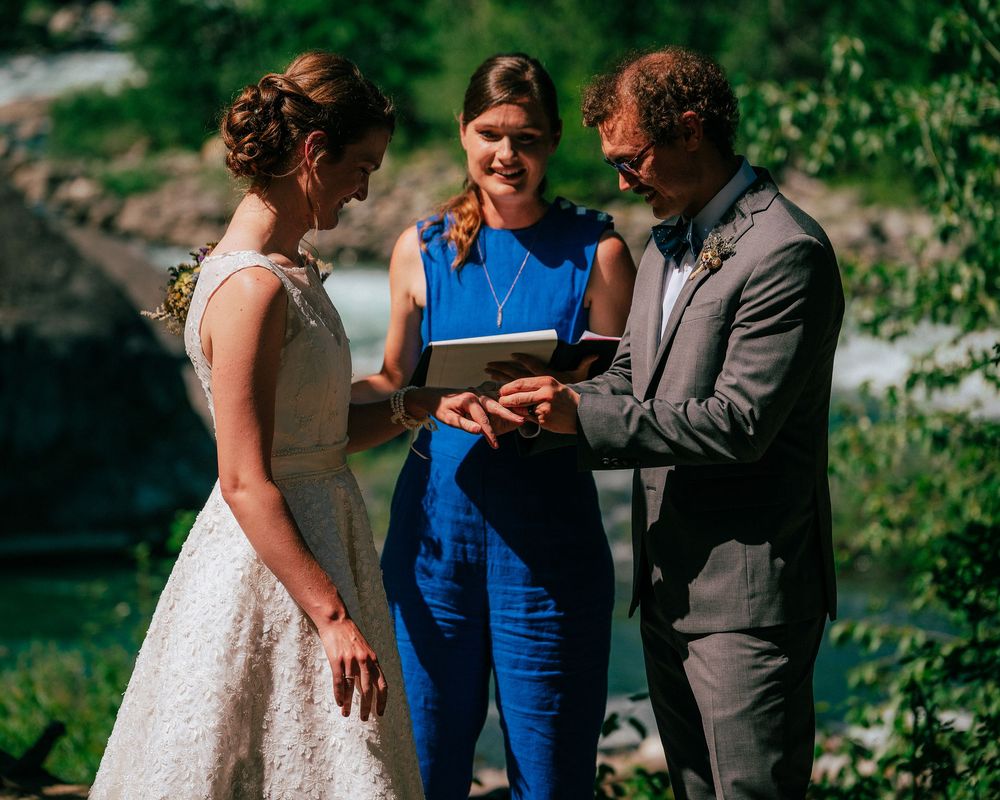 An outdoor wedding ceremony takes place on a dirt path beside a beautiful mountain stream.