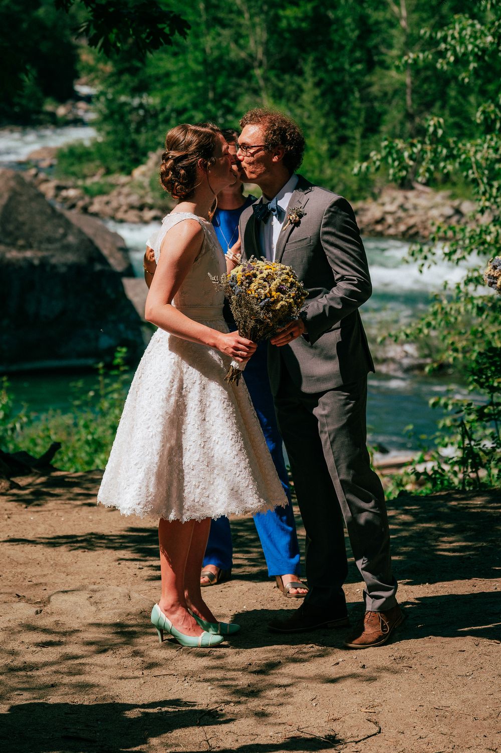 A couple shares an intimate moment during their outdoor wedding beside a rushing river.