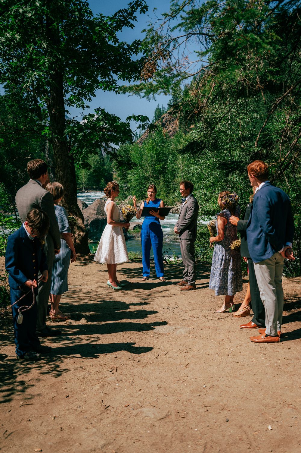 A small gathering of people on a dirt path surrounded by lush green trees on a sunny day.