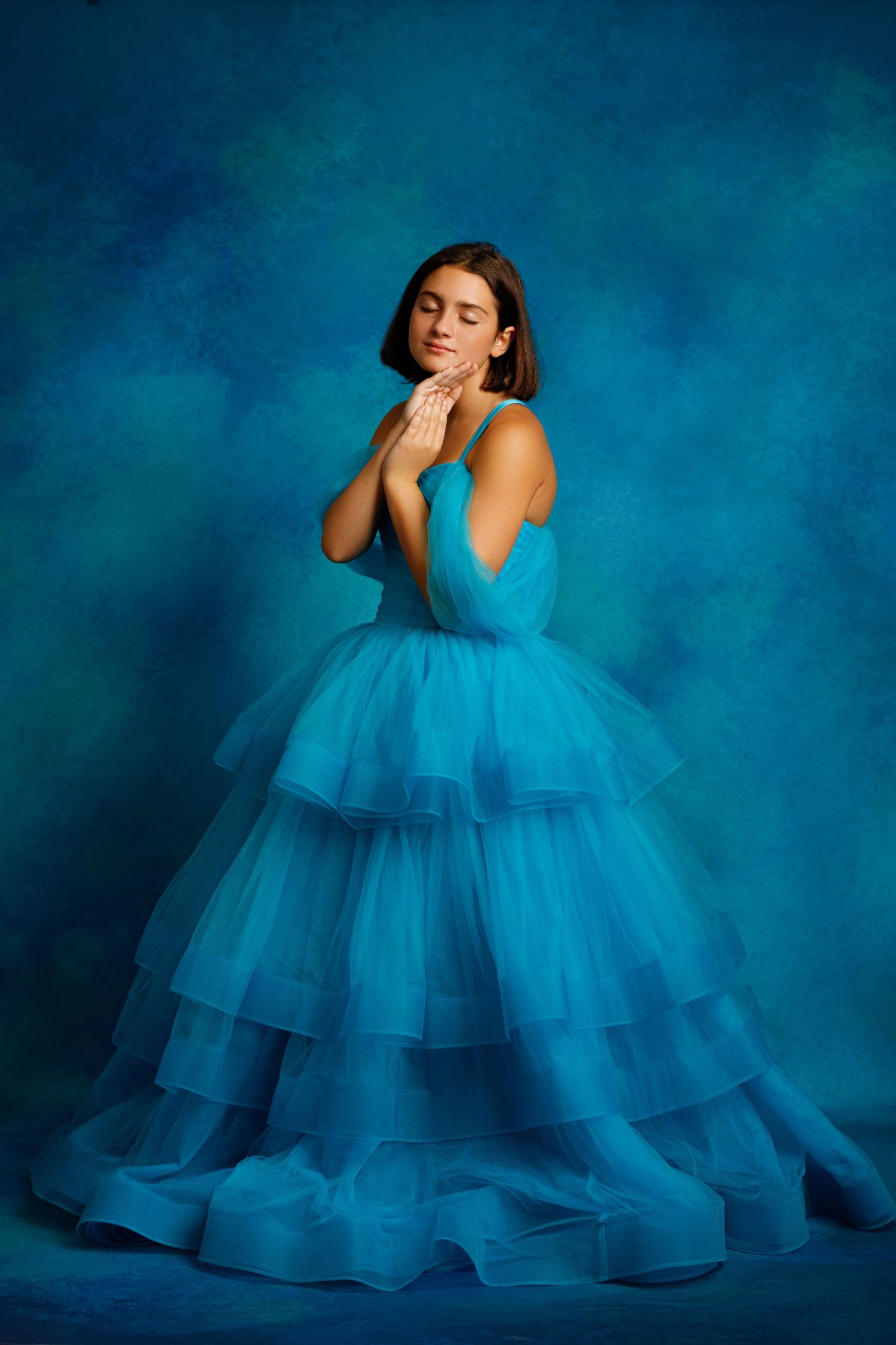Elegant teal ball gown swirls dramatically against a misty blue-gray background in a dreamy portrait session.