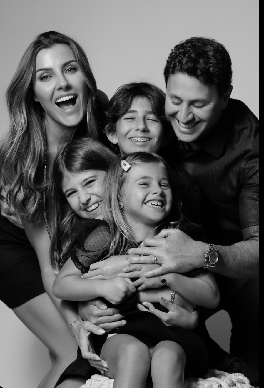 A candid black and white portrait of a happy family of five laughing and hugging together.