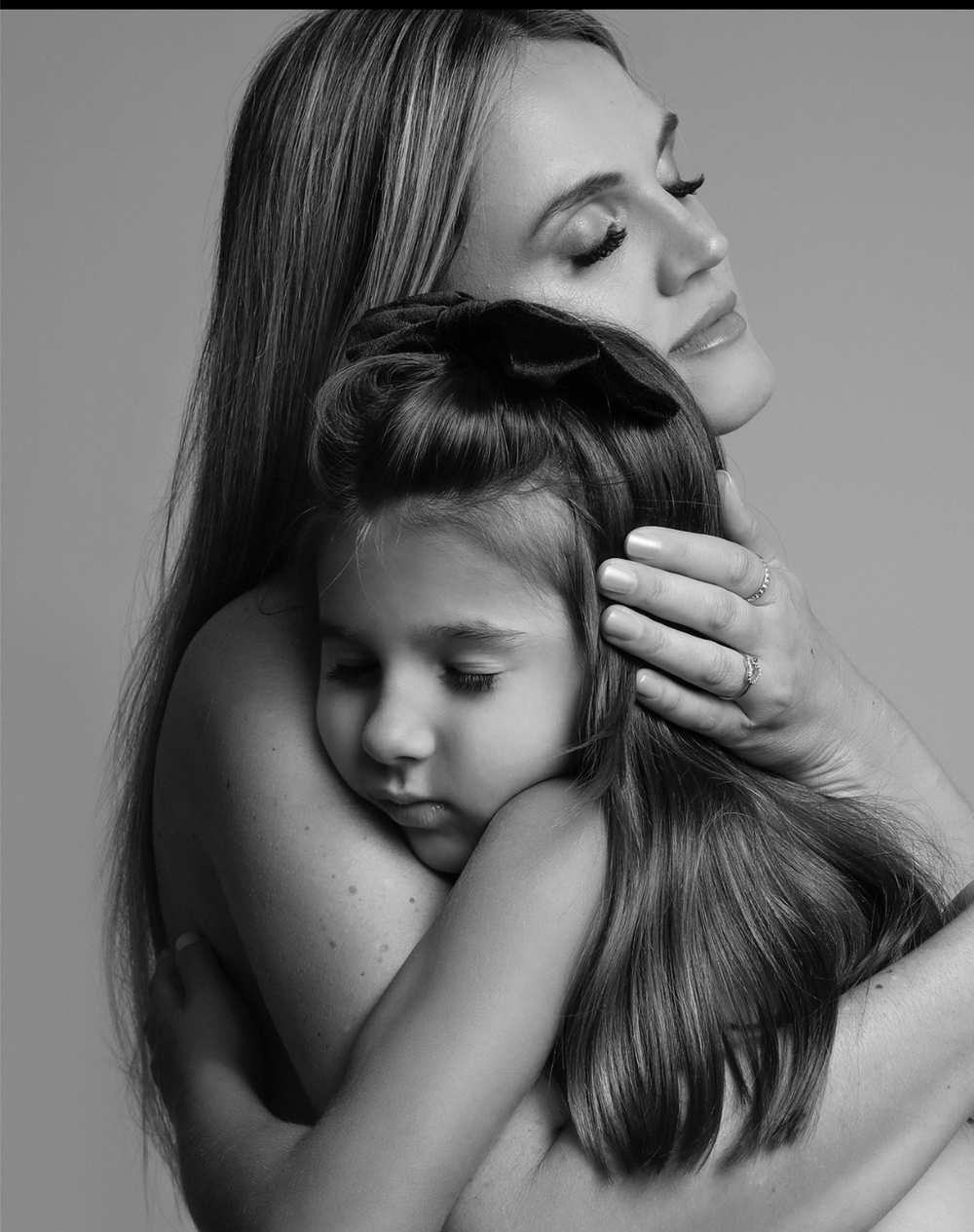 Black and white artistic portrait showing an intimate embrace between parent and child with closed eyes.