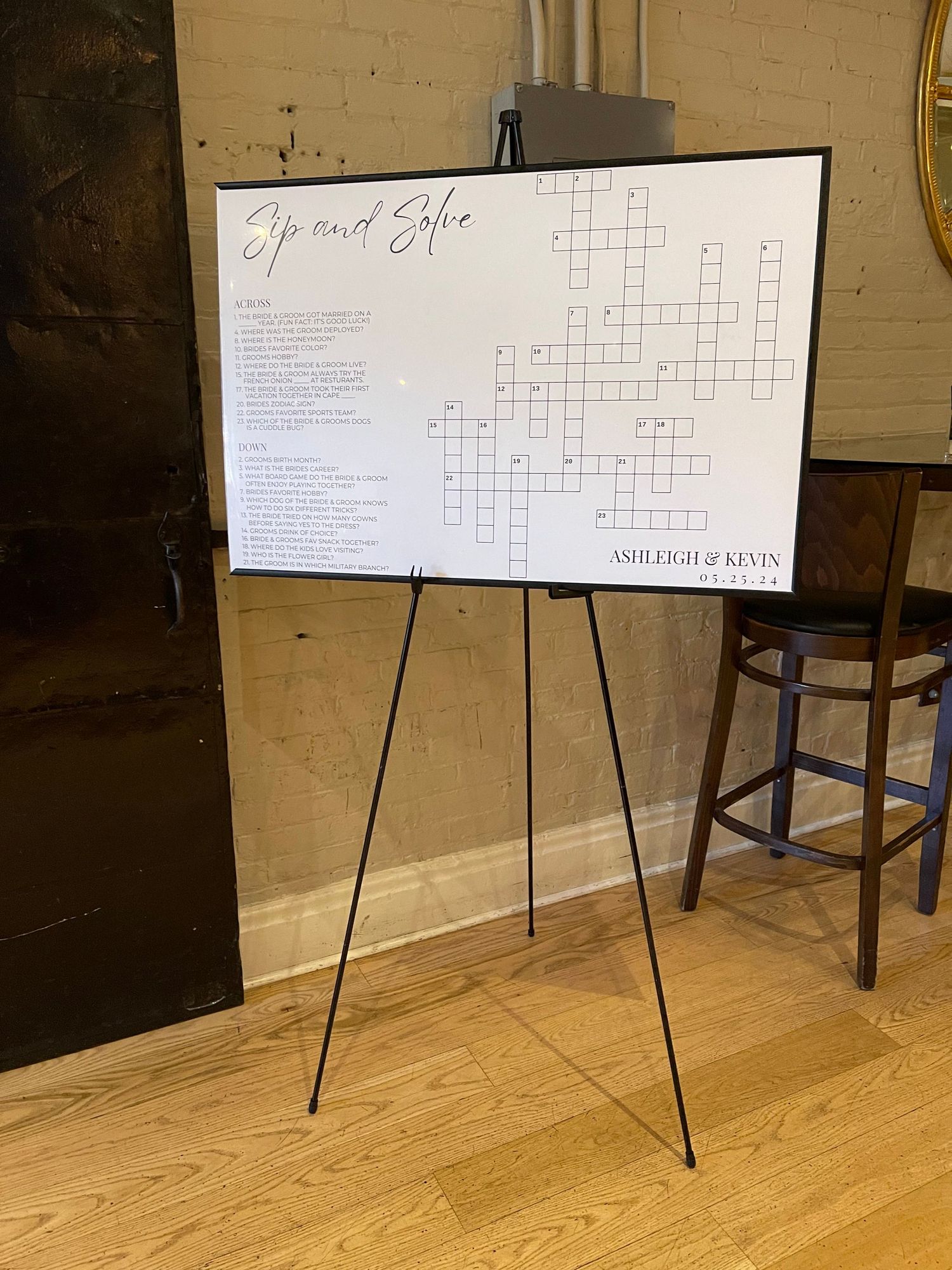 A crossword puzzle displayed on an easel with a white board and wooden frame stands on a hardwood floor.