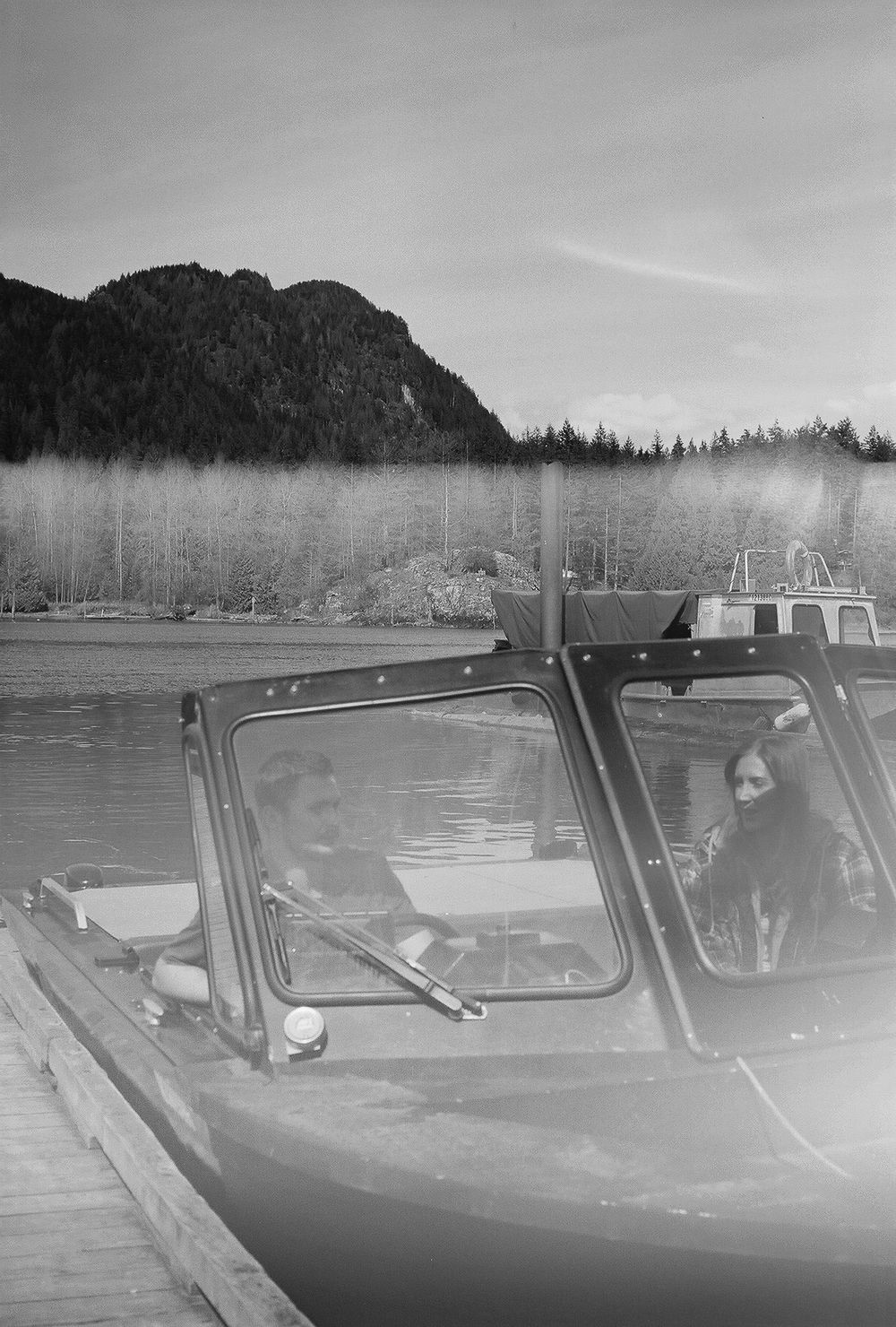 Vintage black and white photograph of cars parked along a waterfront with mountains.