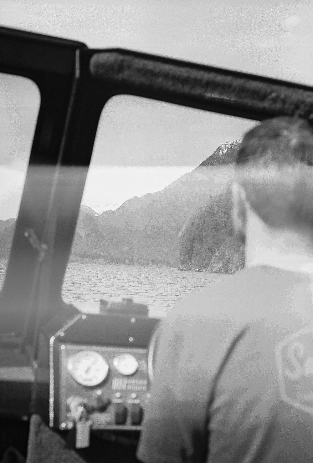 Black and white view of mountains and water through car dashboard.