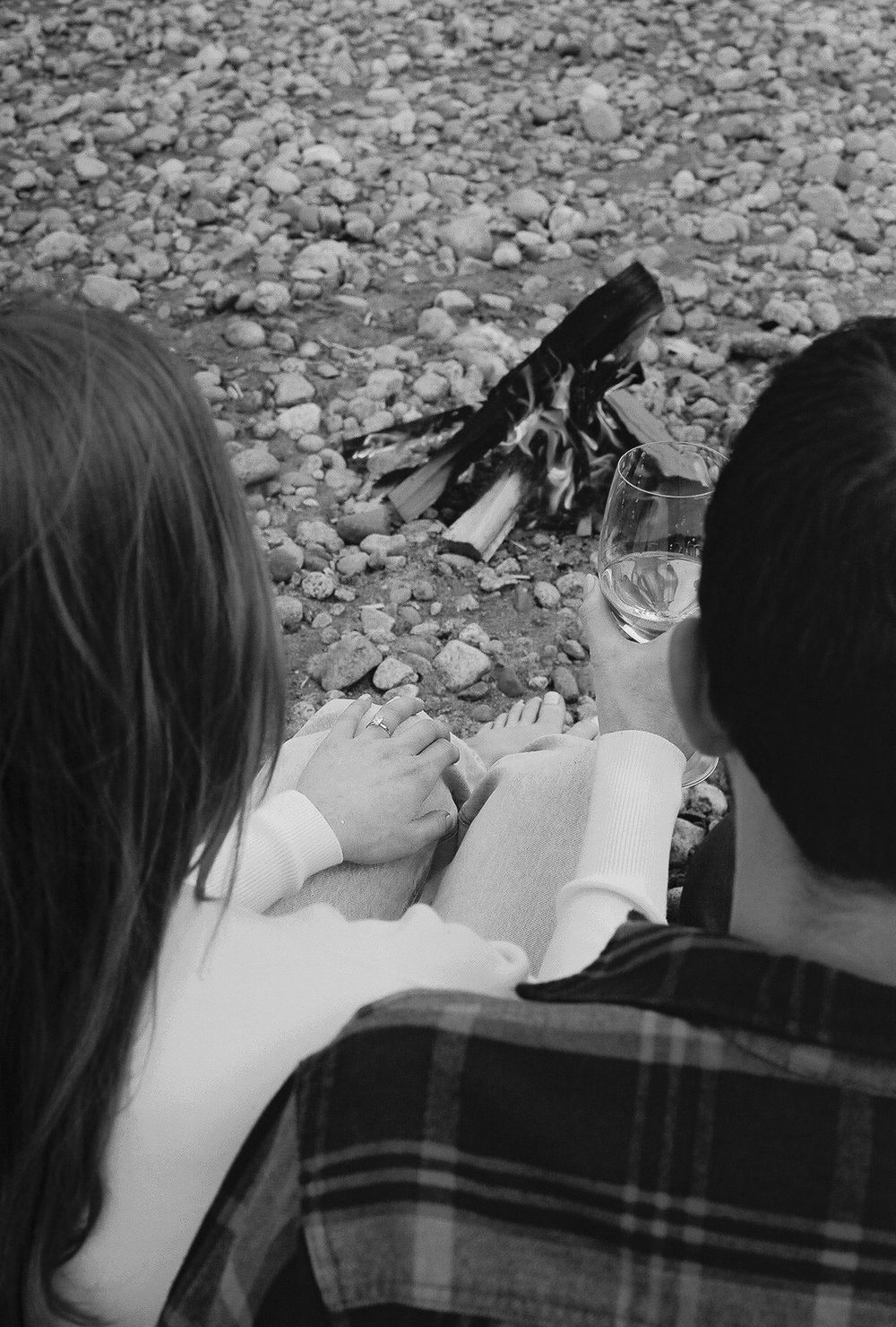 People sitting on rocky beach looking out at mountain vista in black and white.