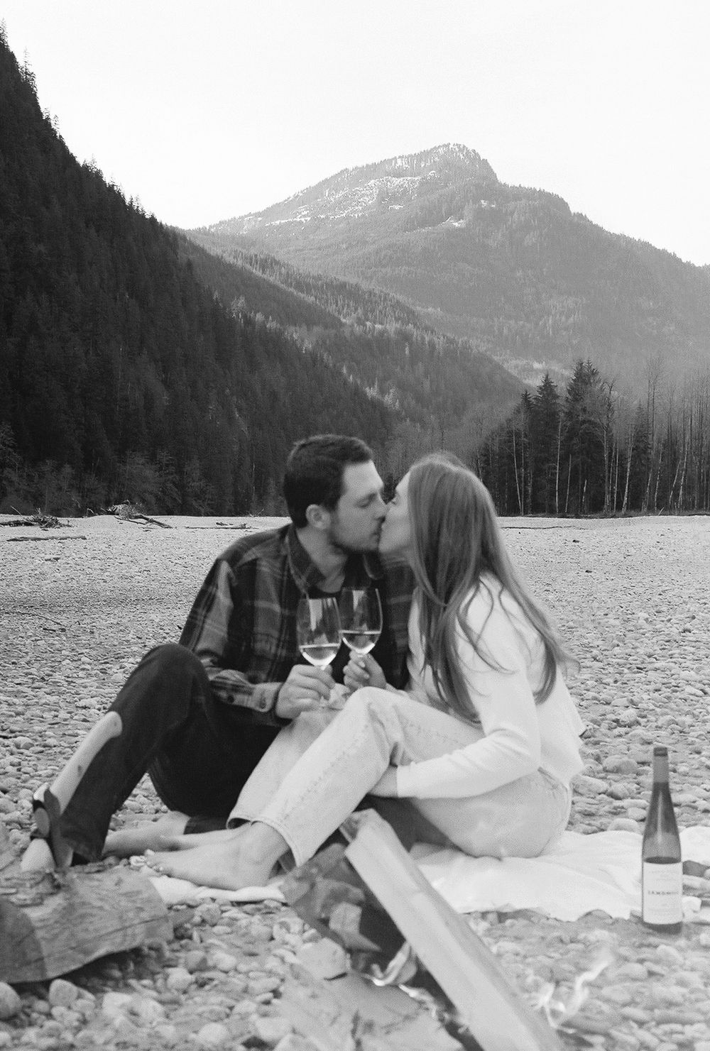 Couple having picnic on rocky beach with mountains in background.