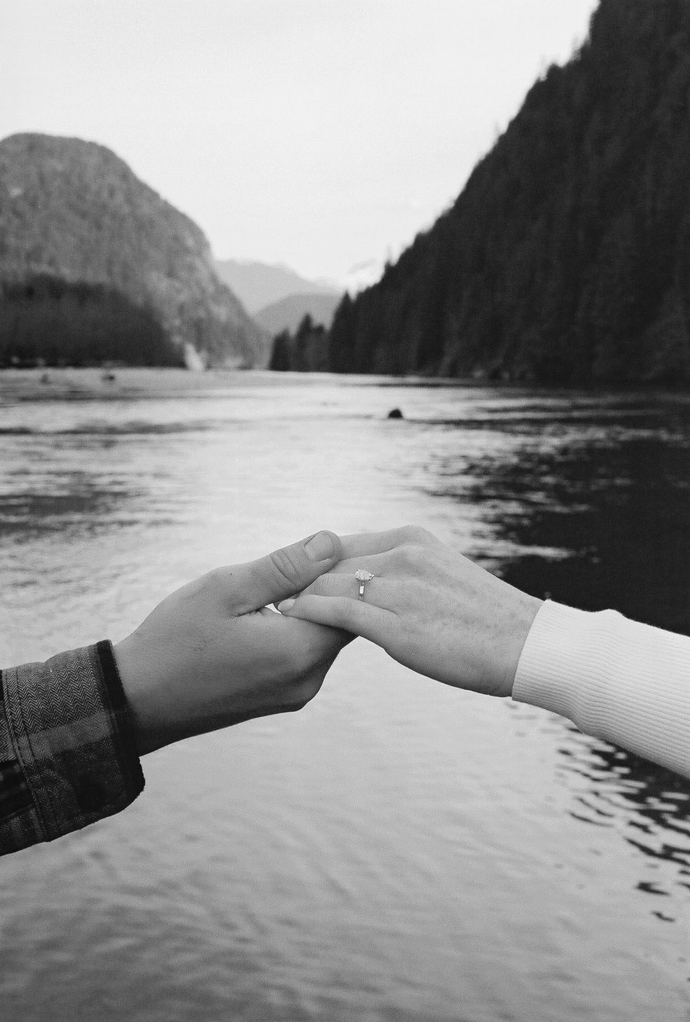 Reaching hands silhouetted against a mountain lake landscape.