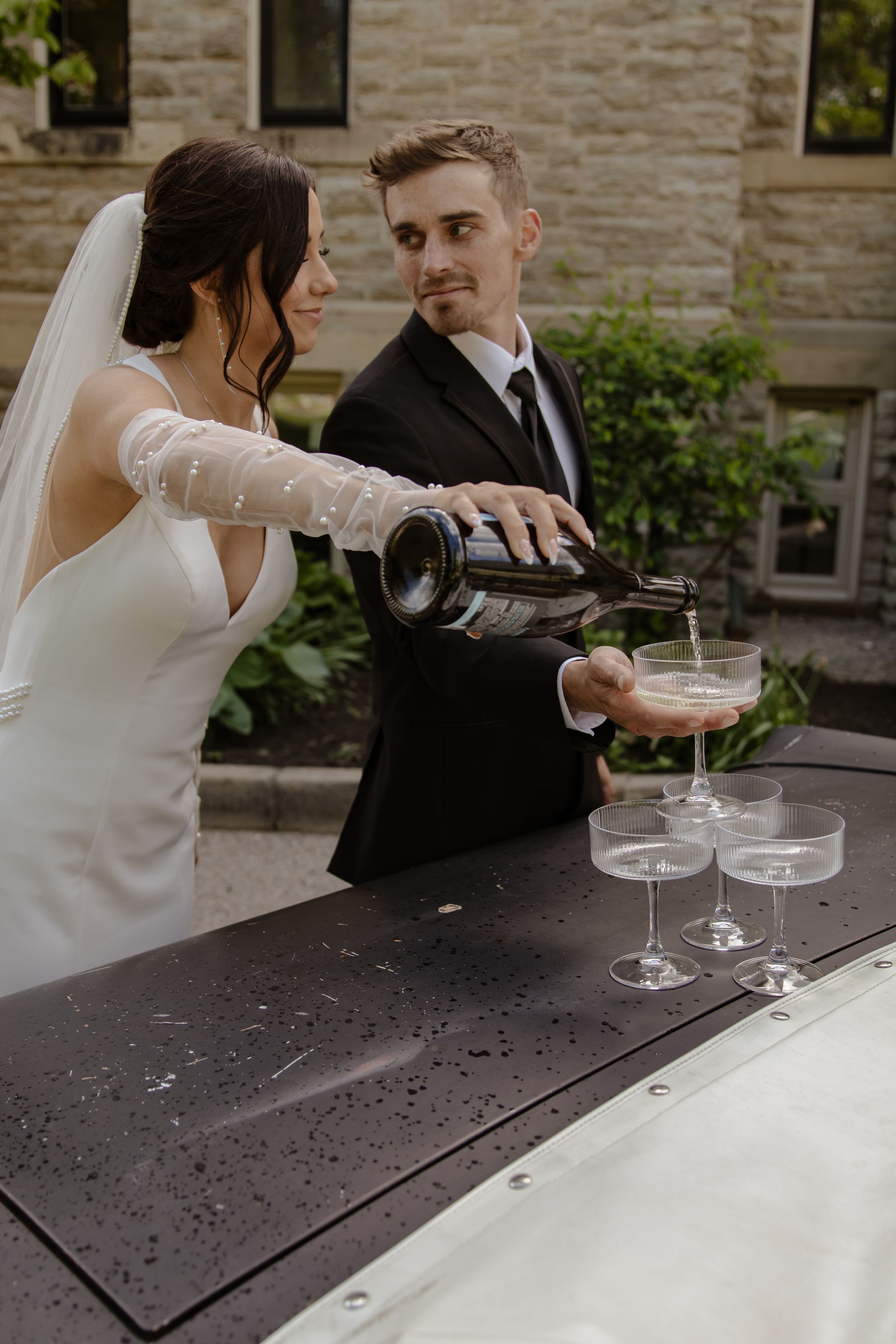 Wedding couple sharing champagne on a classic car hood.