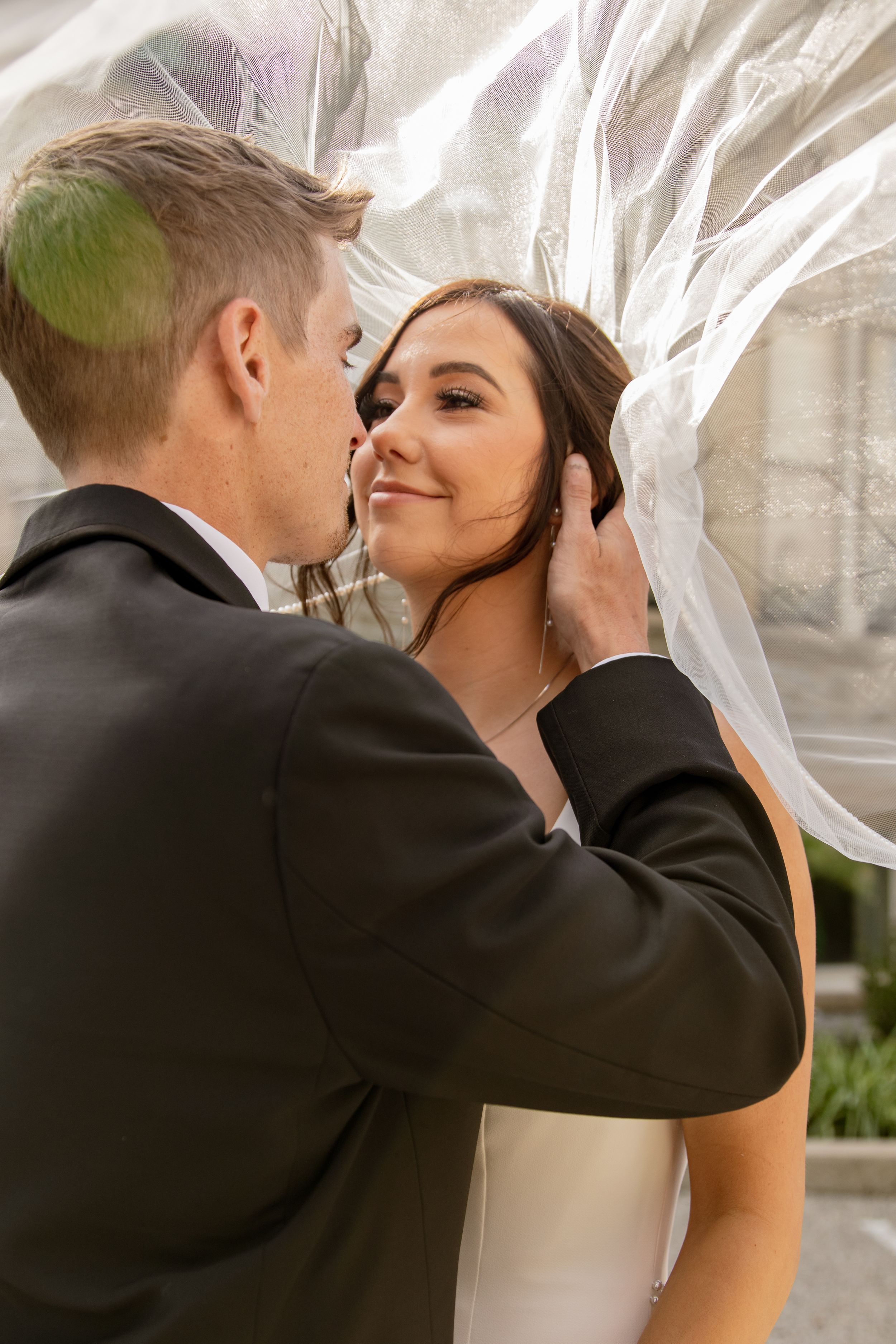 Romantic moment between newlyweds under flowing veil.