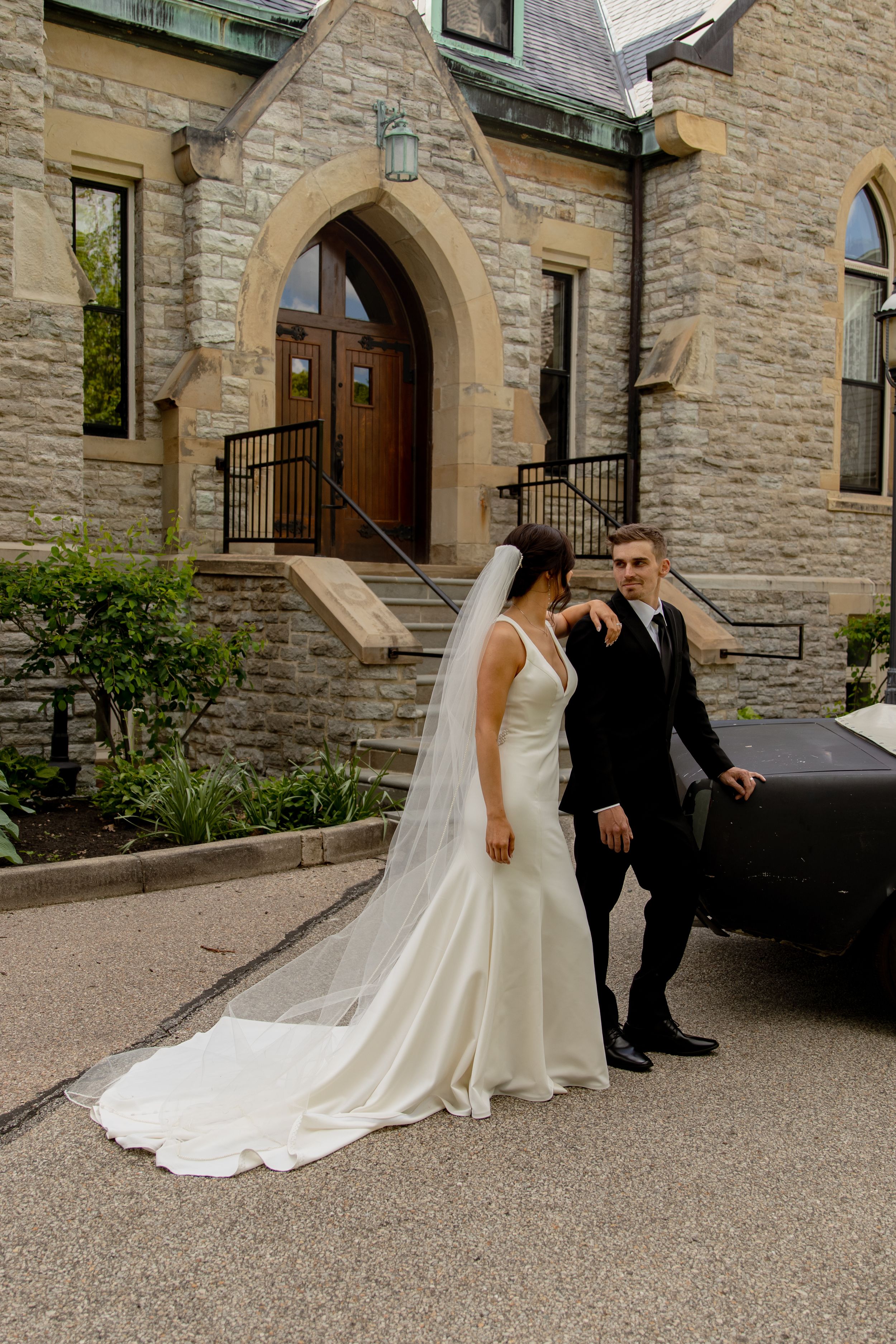 Elegant couple poses by stone church entrance with flowing wedding dress.