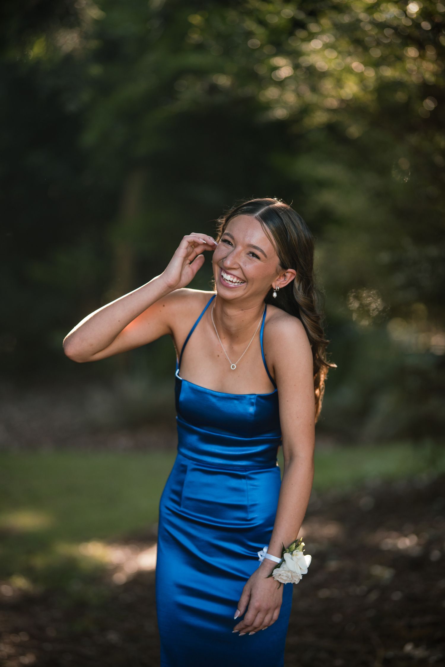 A girl in a blue formal dress laughing, with a white corsage on her wrist