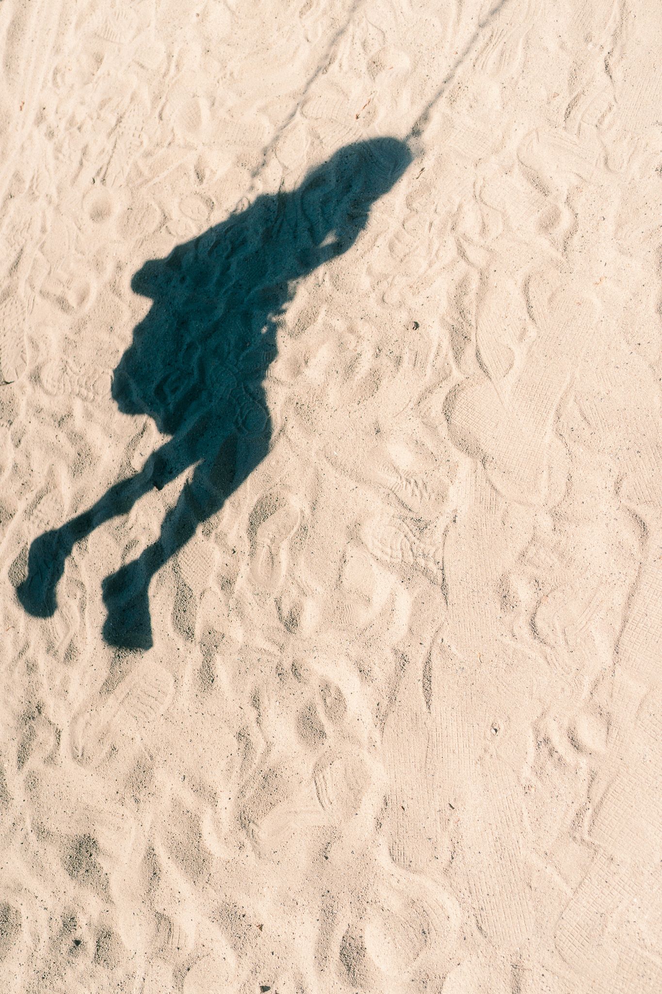 The shade of a child on the sand as they are on a swing.