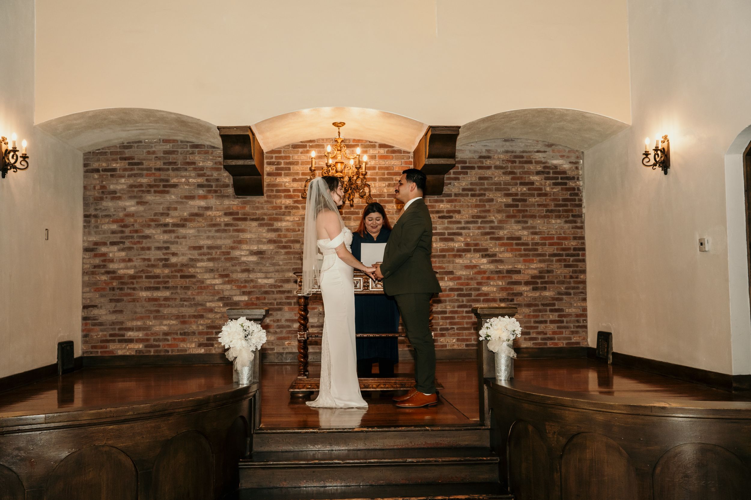 A couple sharing a romantic moment at their wedding ceremony on rustic wooden steps with stone walls and warm lighting.