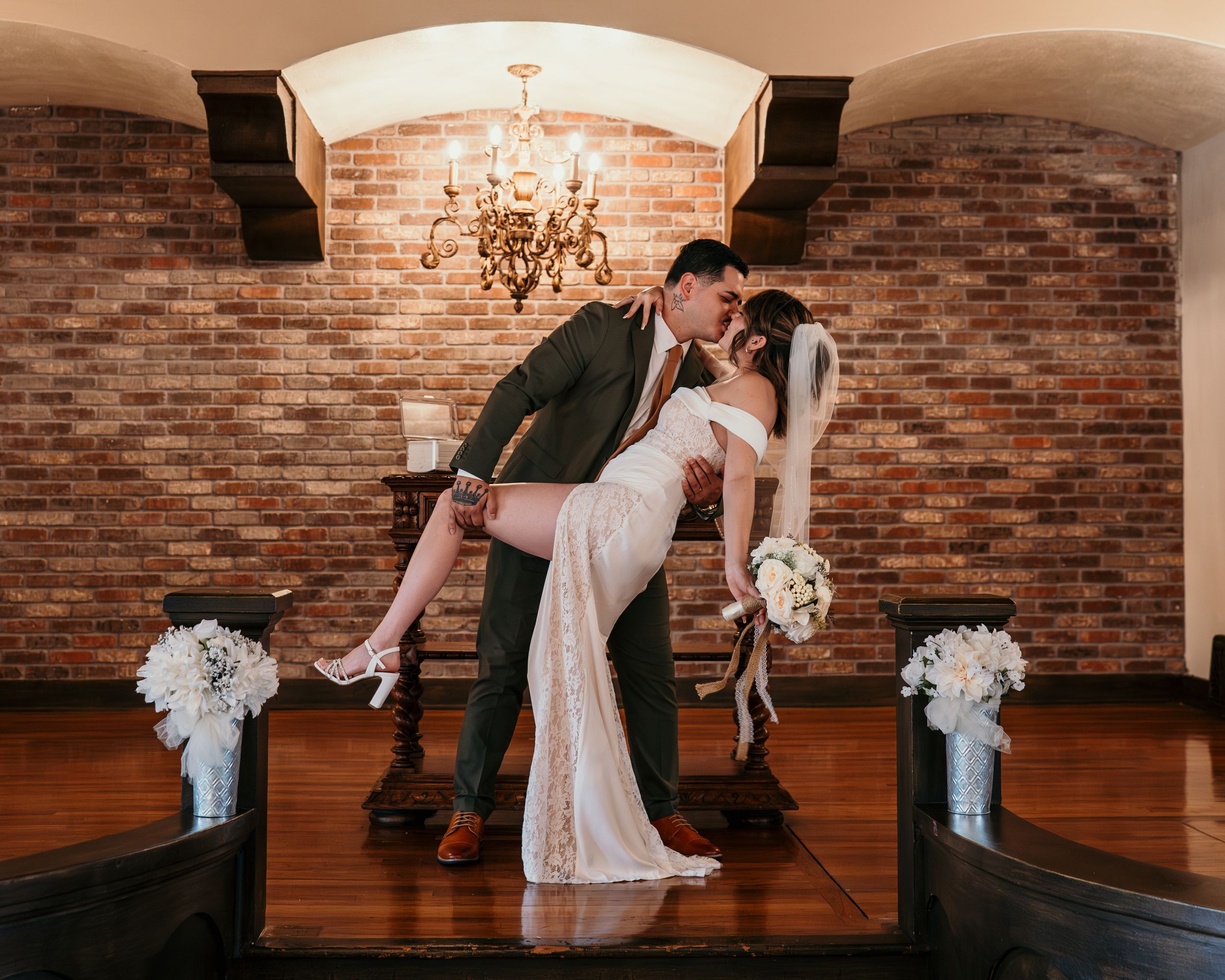 A romantic dance moment between two people in an elegant venue with brick walls and a chandelier overhead.