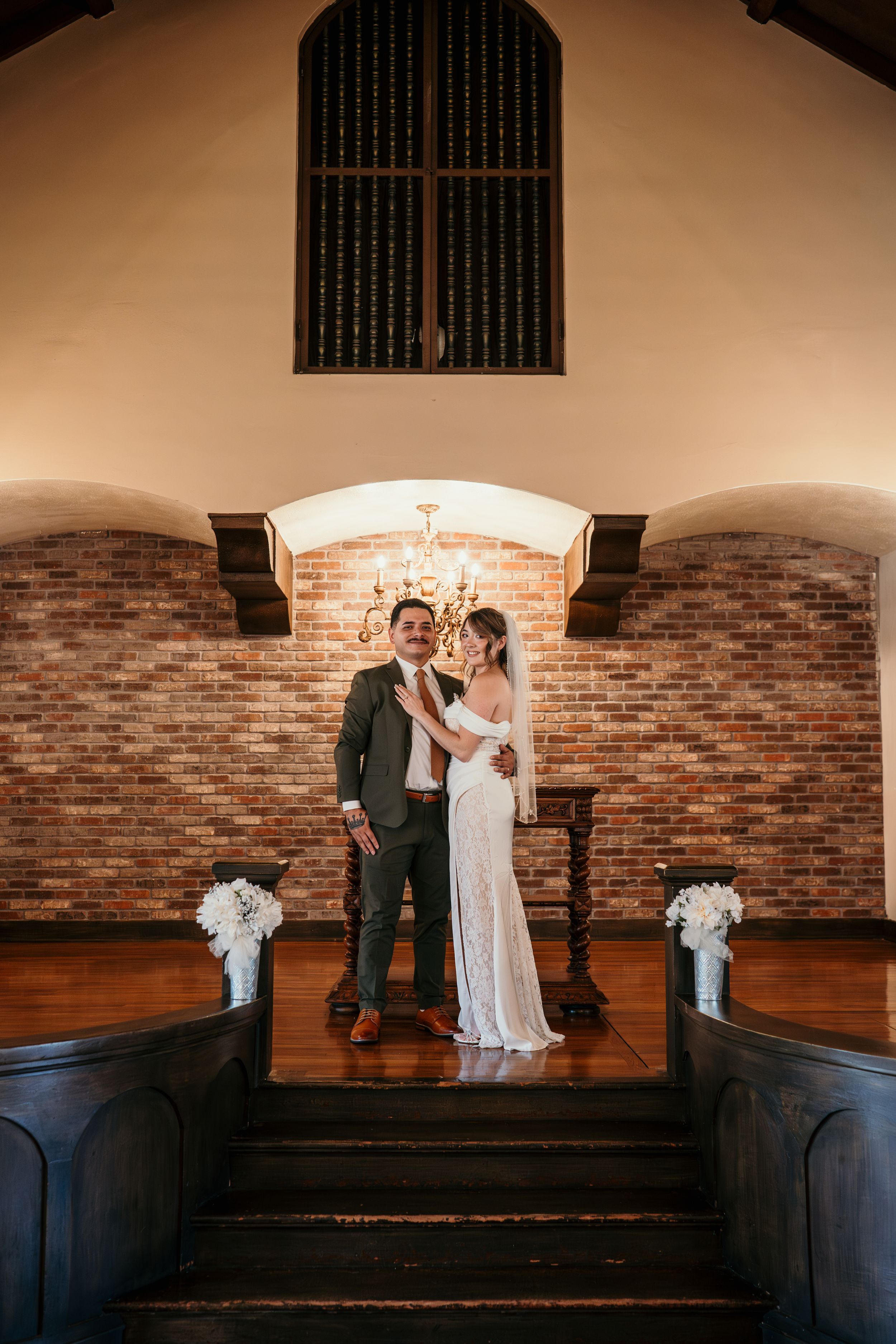 A romantic wedding scene inside a historic brick chapel with wood floors and arched windows.