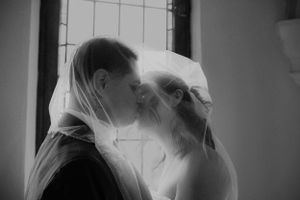 A blurred black and white photo shows two people in wedding attire sharing an intimate moment under a veil.