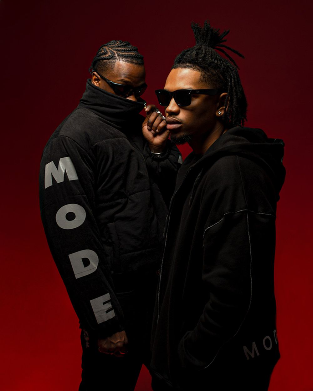 Two figures in black hoodies pose against a deep red backdrop, with one wearing sunglasses and the other displaying MODE text.