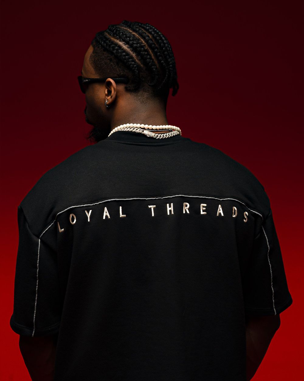 Back view of black t-shirt with LOYAL THREADS text against deep red backdrop.