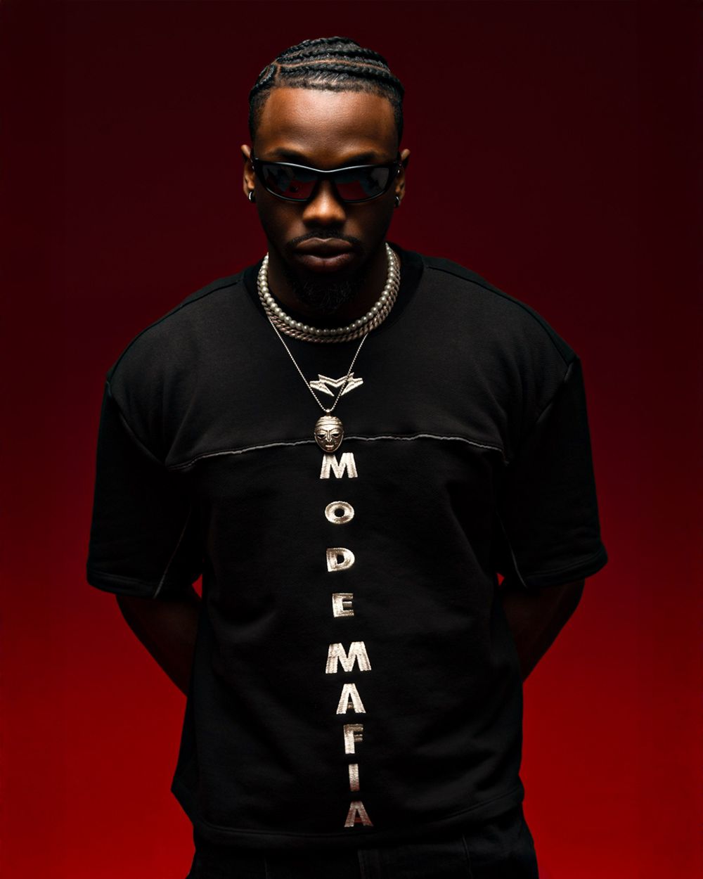 Stylish portrait against dark red background wearing black t-shirt with vertical text and gold chain necklaces.