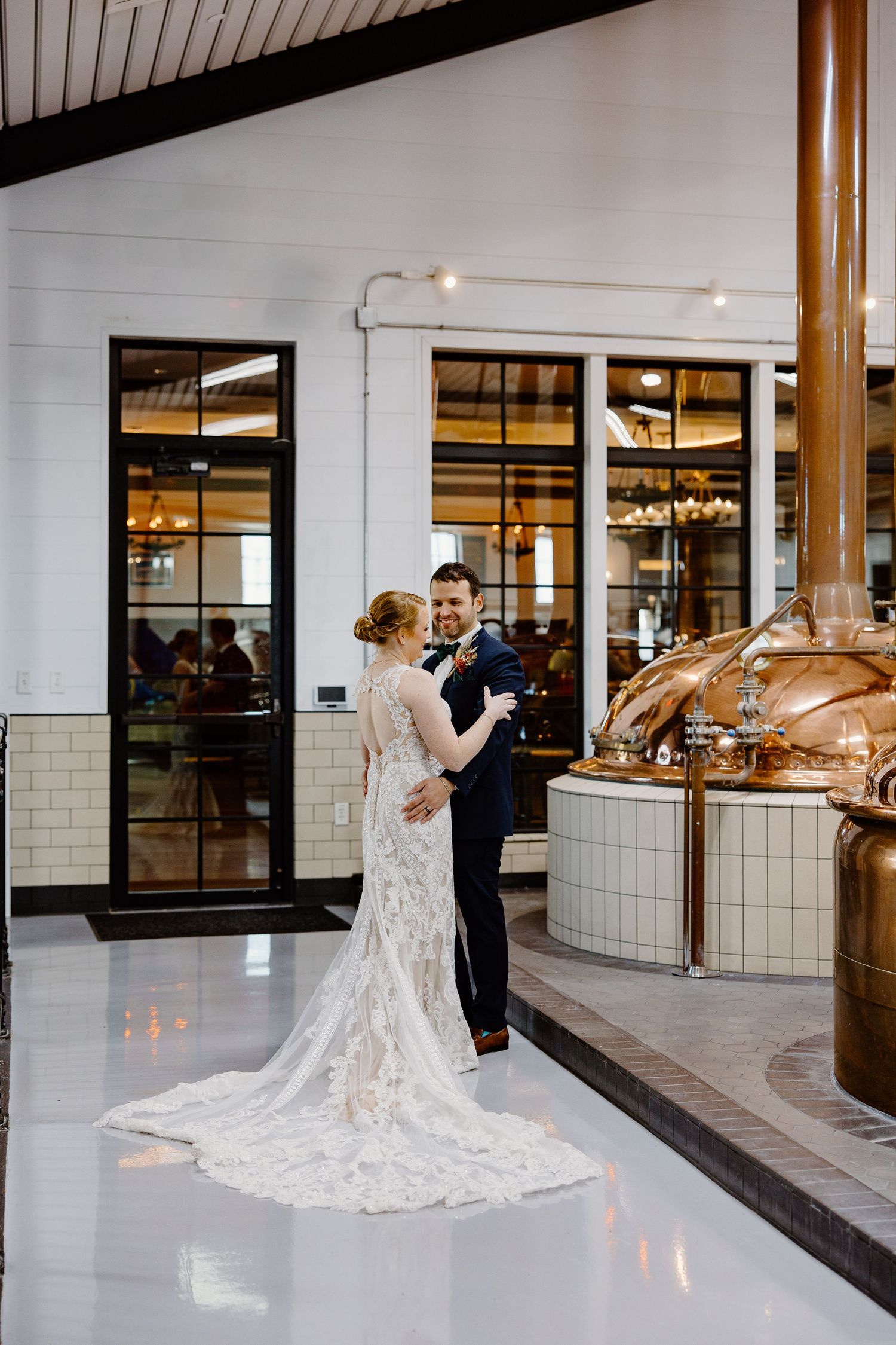 Sequence of wedding photos showing elegant couple dancing in spacious industrial-style venue with copper brewing tanks.