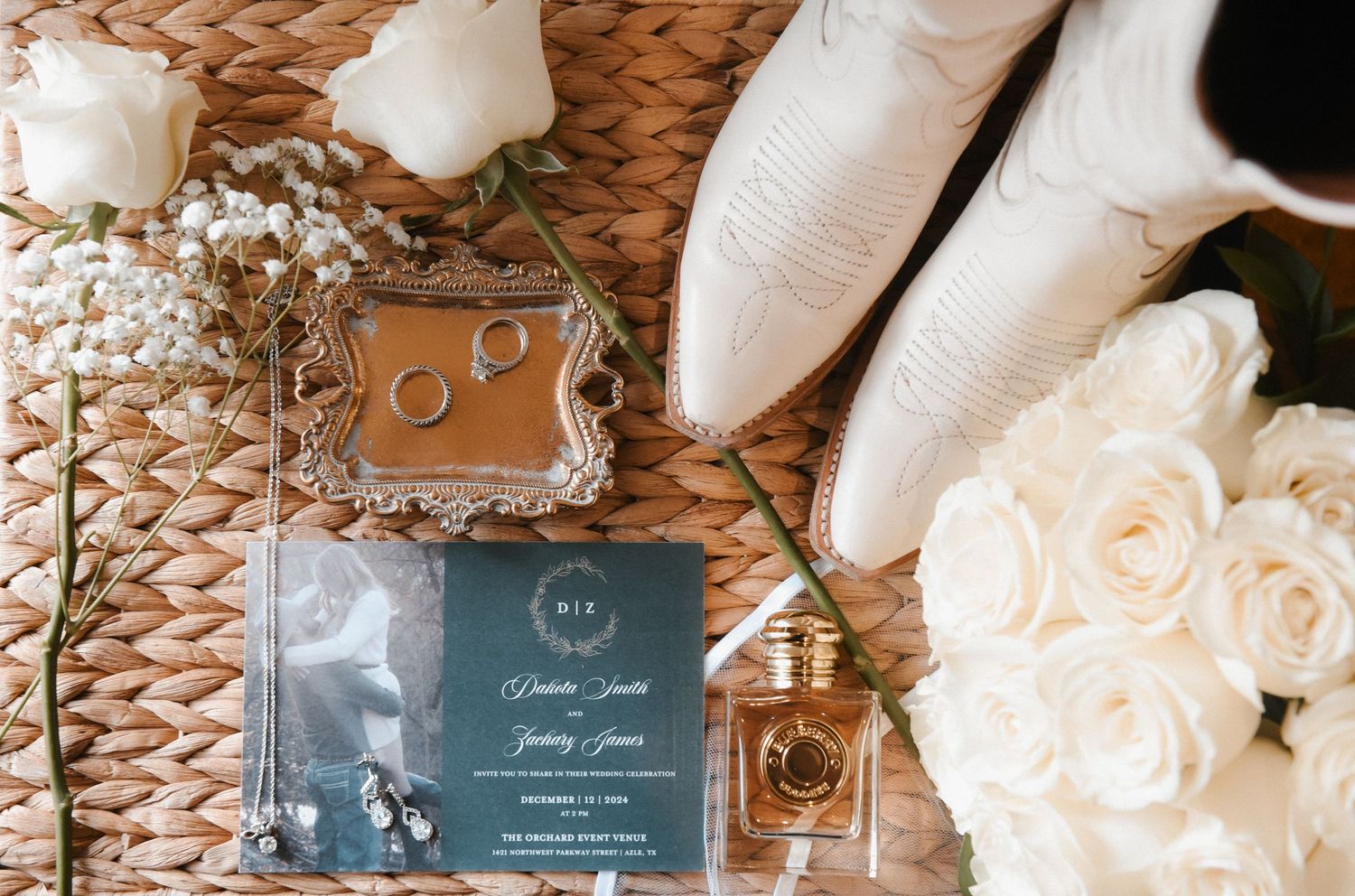 Wedding details layout featuring white roses, golden rings, and invitation cards on a woven textured background.