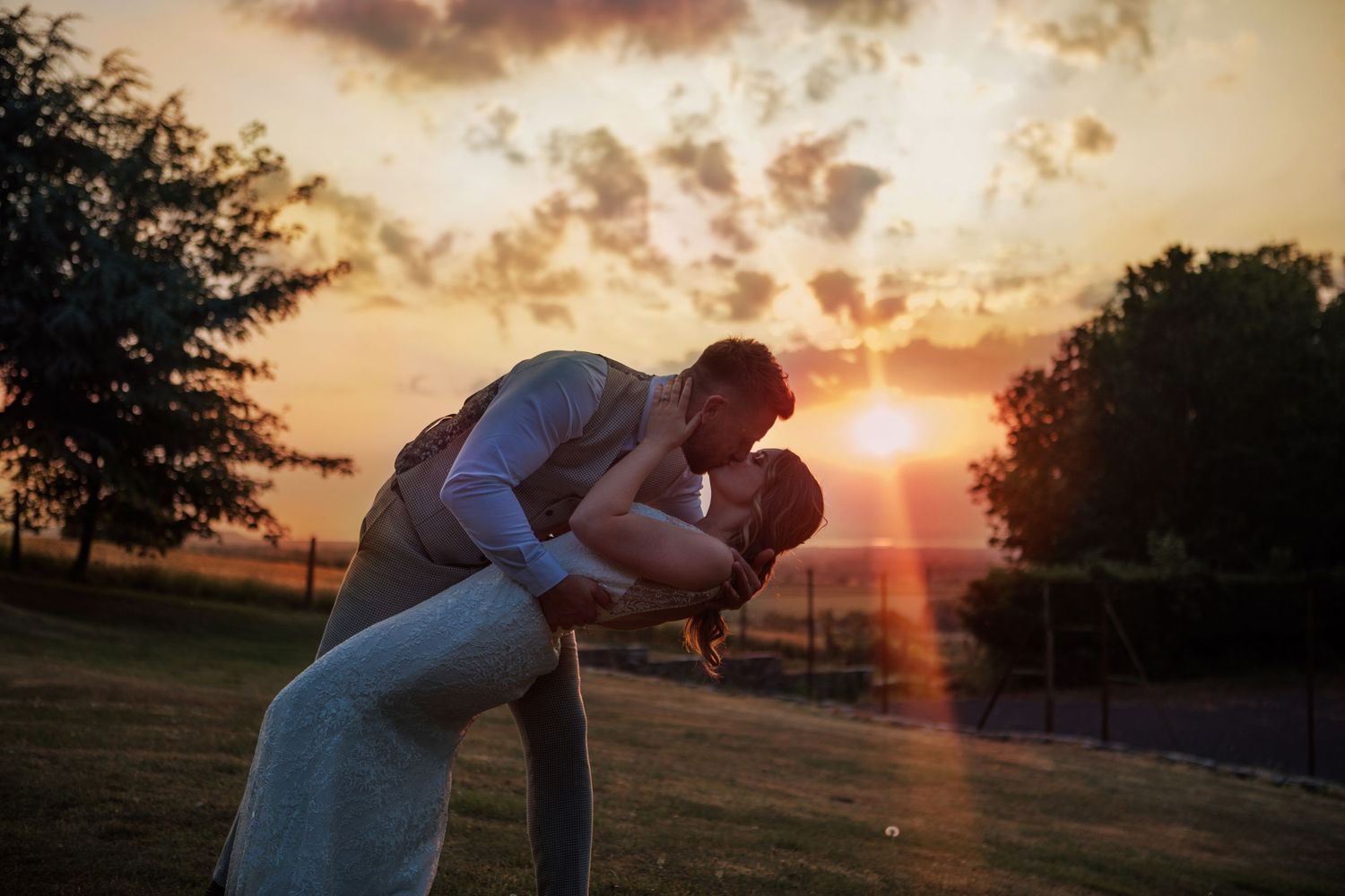 A couple walks hand in hand through a grassy meadow on their wedding day, with the bride wearing a detailed floral dress.