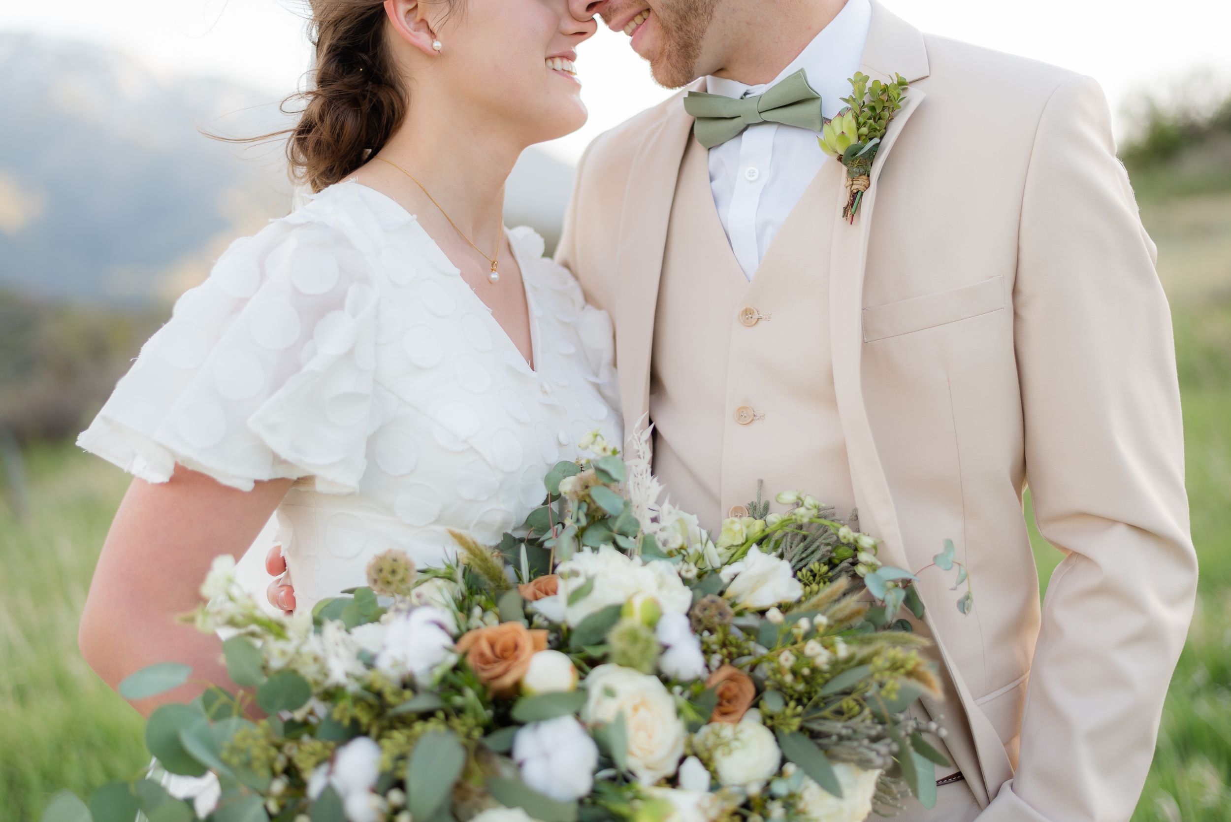 Bride and groom share a romantic moment, she holds a lush bouquet of white and peach flowers with greenery. Megan Snell Photo Utah Weddings
