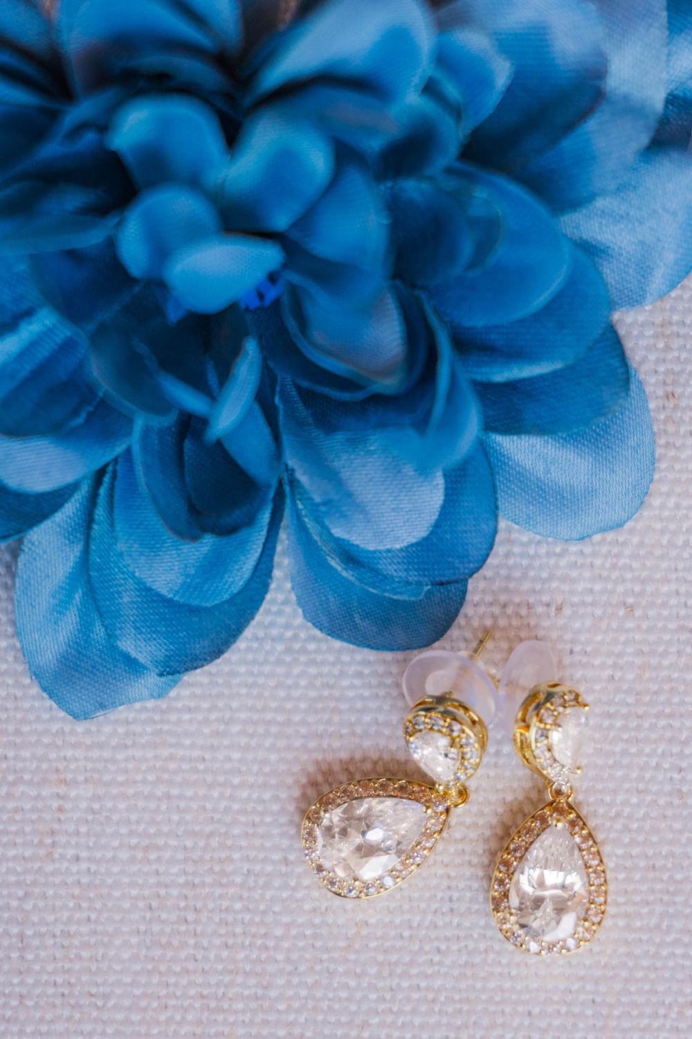 Blue silk flower with crystal teardrop earrings on white textured background.