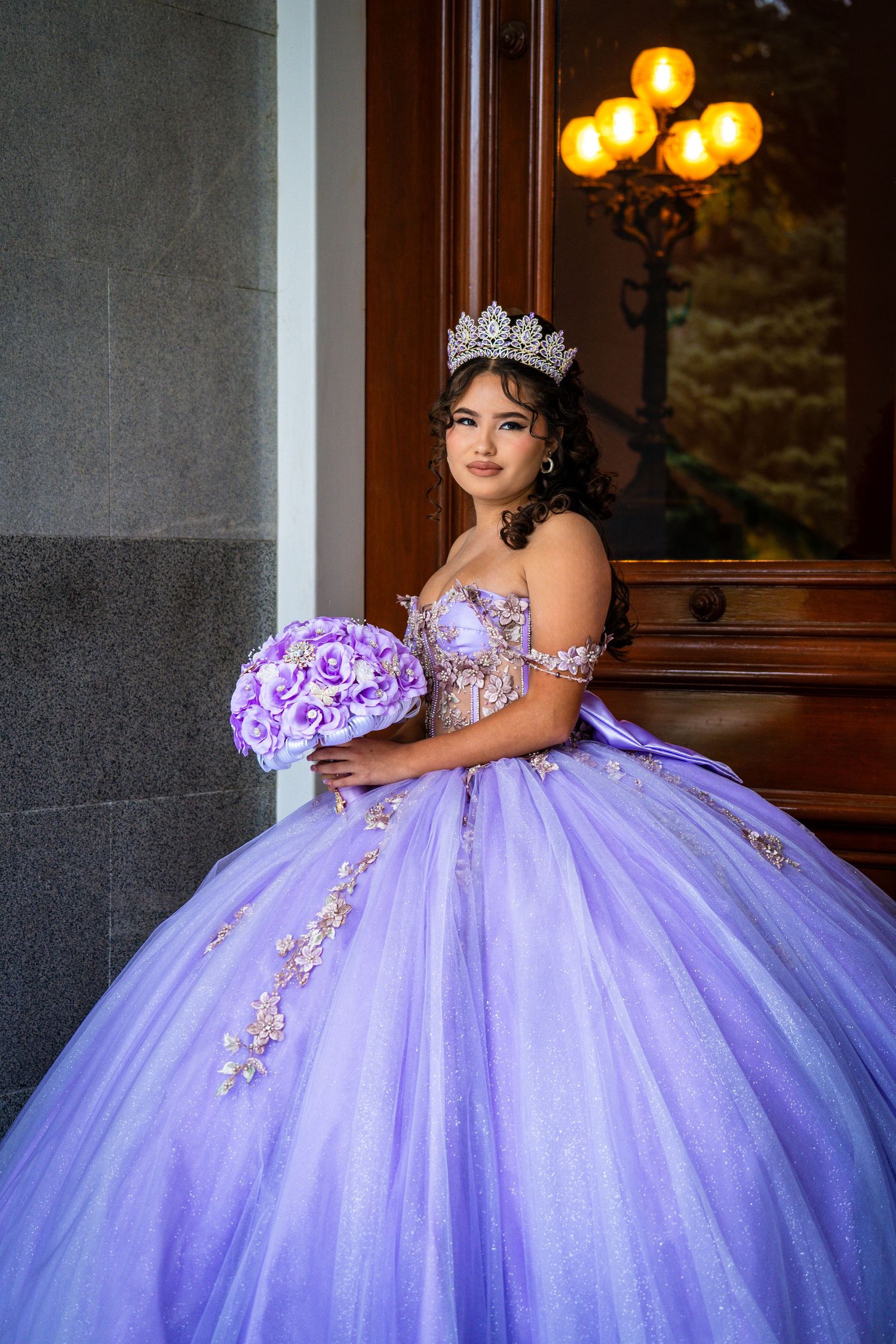 Woman in purple ball gown holding bouquet by vintage doorway.