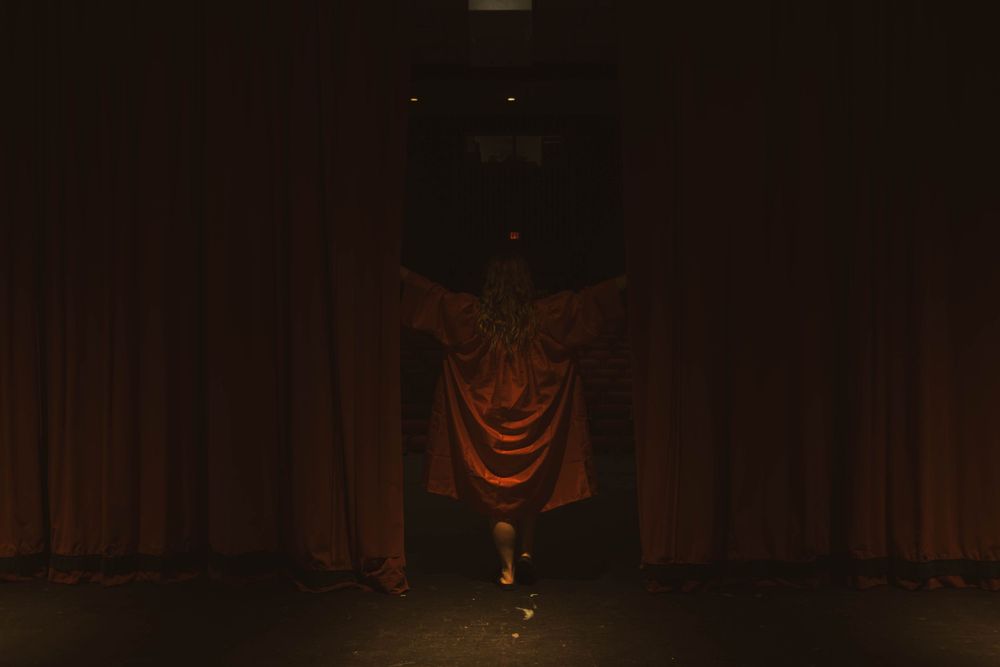 Dark theater space with red-lit figures creating mysterious shadows.