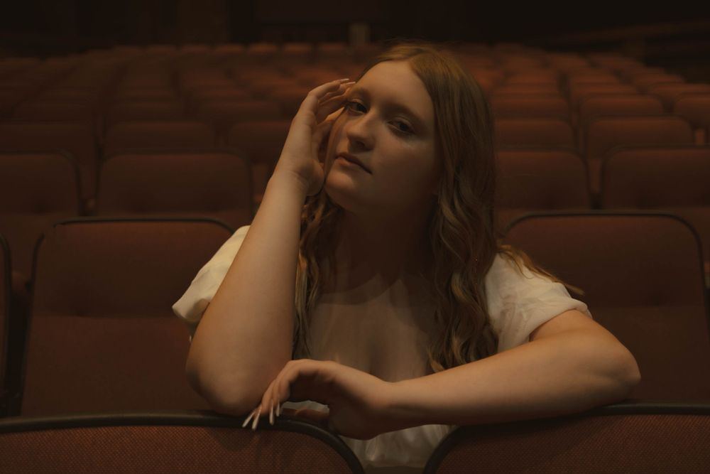 Theatrical scene in warm lighting showing dramatic poses in theater seating.