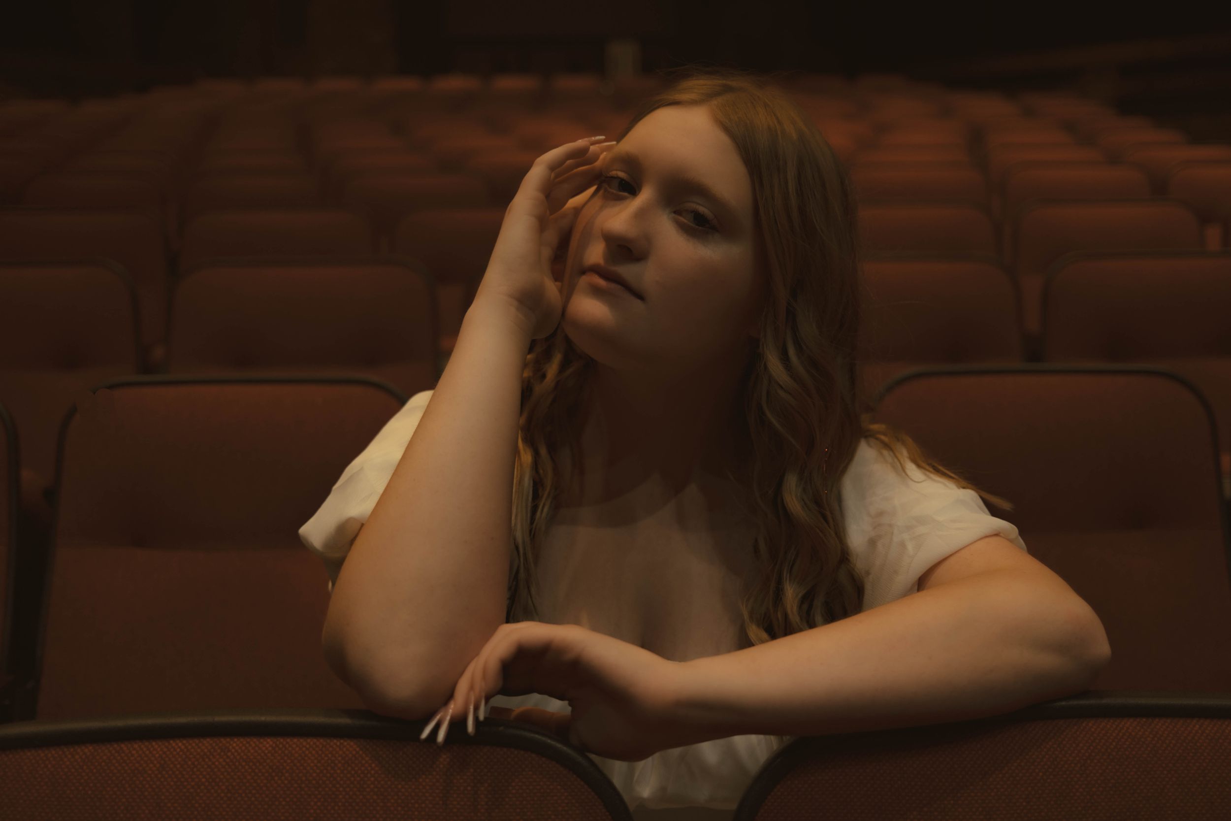 Theatrical scene in warm lighting showing dramatic poses in theater seating.