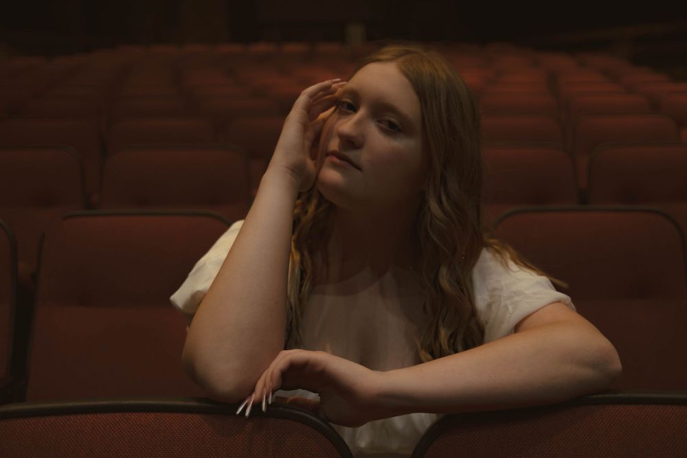 A person lounges on a brown leather couch in a dimly lit room with dramatic lighting.