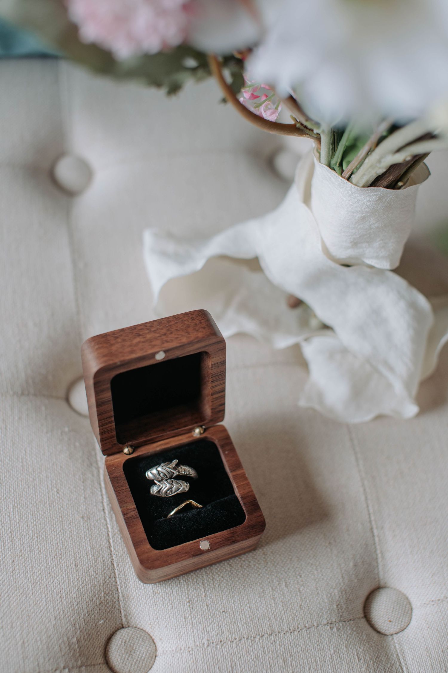Wedding rings displayed in wooden box with white fabric and floral decoration.