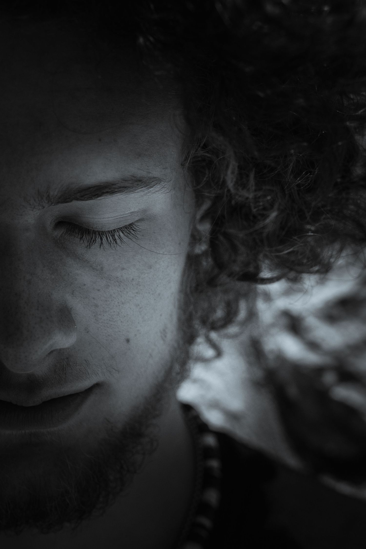 Profile view of person with curly hair in contemplative pose against green foliage.