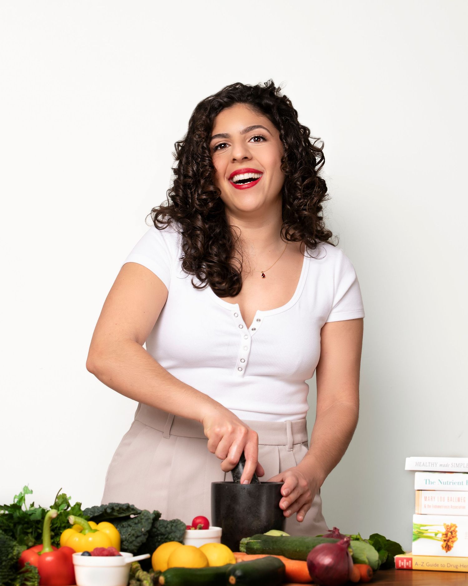 Cook in white top prepares fresh ingredients on counter with colorful produce and kitchen tools.
