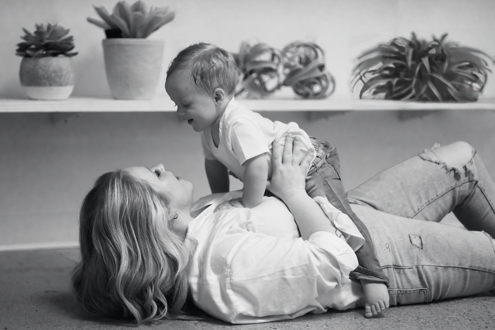 Black and white tender moment on floor capturing parent and child playing at home with potted succulents in background.