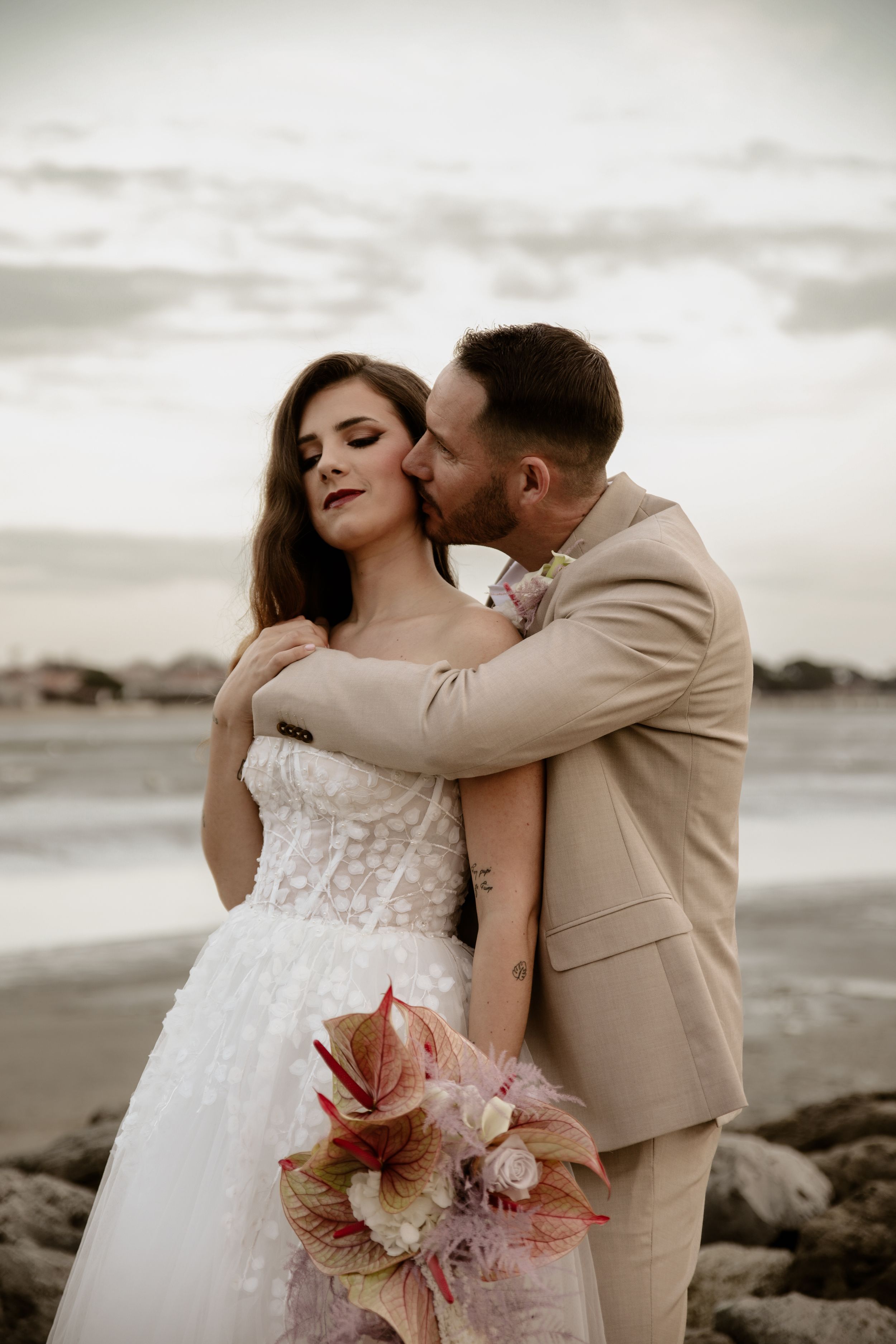 Romantic moment between newlyweds on beach with bride holding pink floral bouquet.