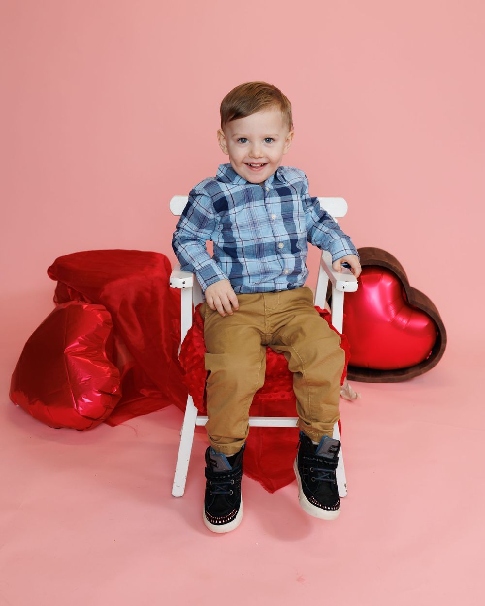 Sweet Valentine's portrait of young child on white chair with red heart balloons and pink background.