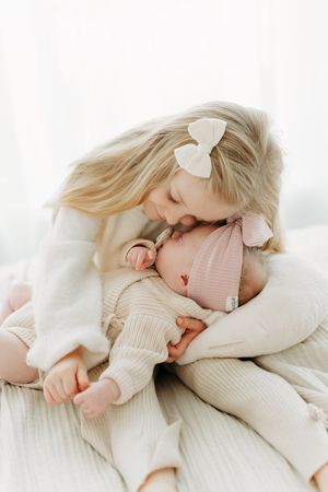 Grande soeur et bébé naissant tout habillé en crème et blanc partageant un moment de tendresse au studio de Québec