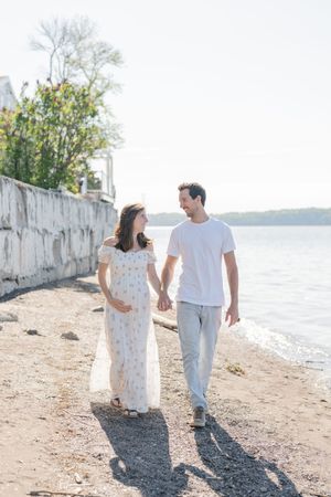 Couple de futurs parents marchant main dans la main sur la plage à Cap-Rouge, Québec, pour une séance photo de maternité au bord du fleuve