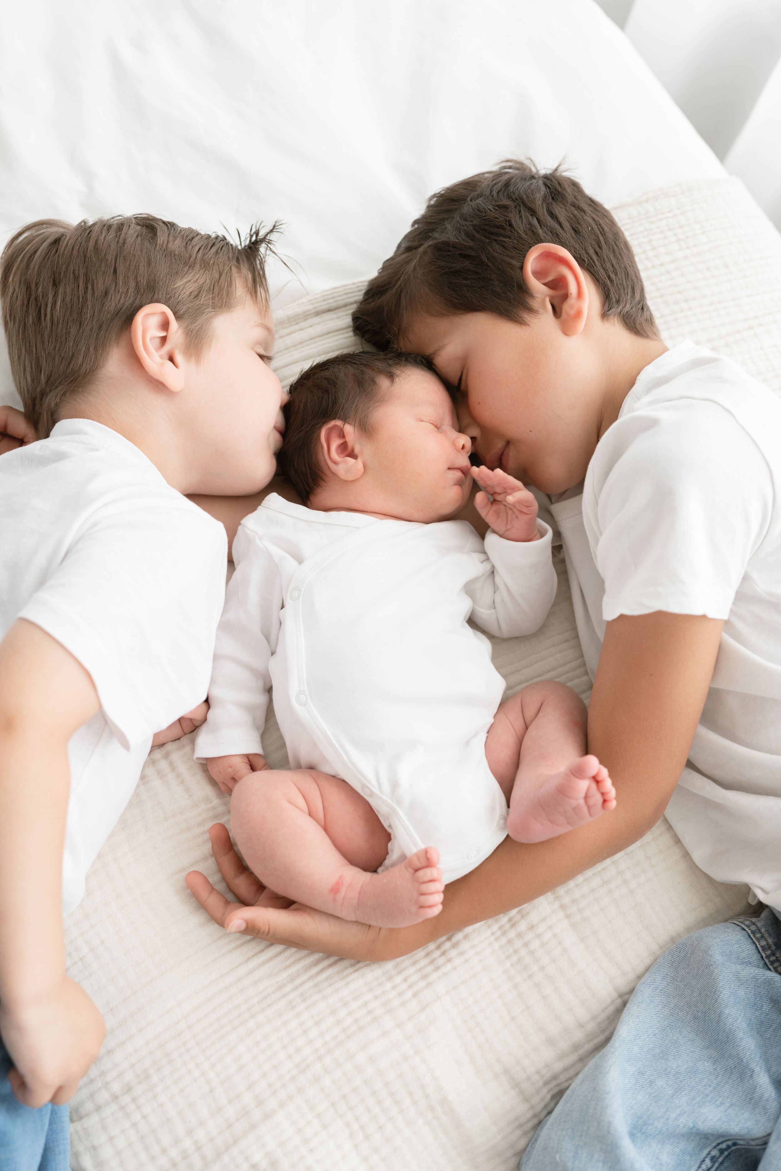 Grands frères et leur petit frère nouveau-né partageant un doux moment lors d'une séance photo nouveau-né au studio près de Québec