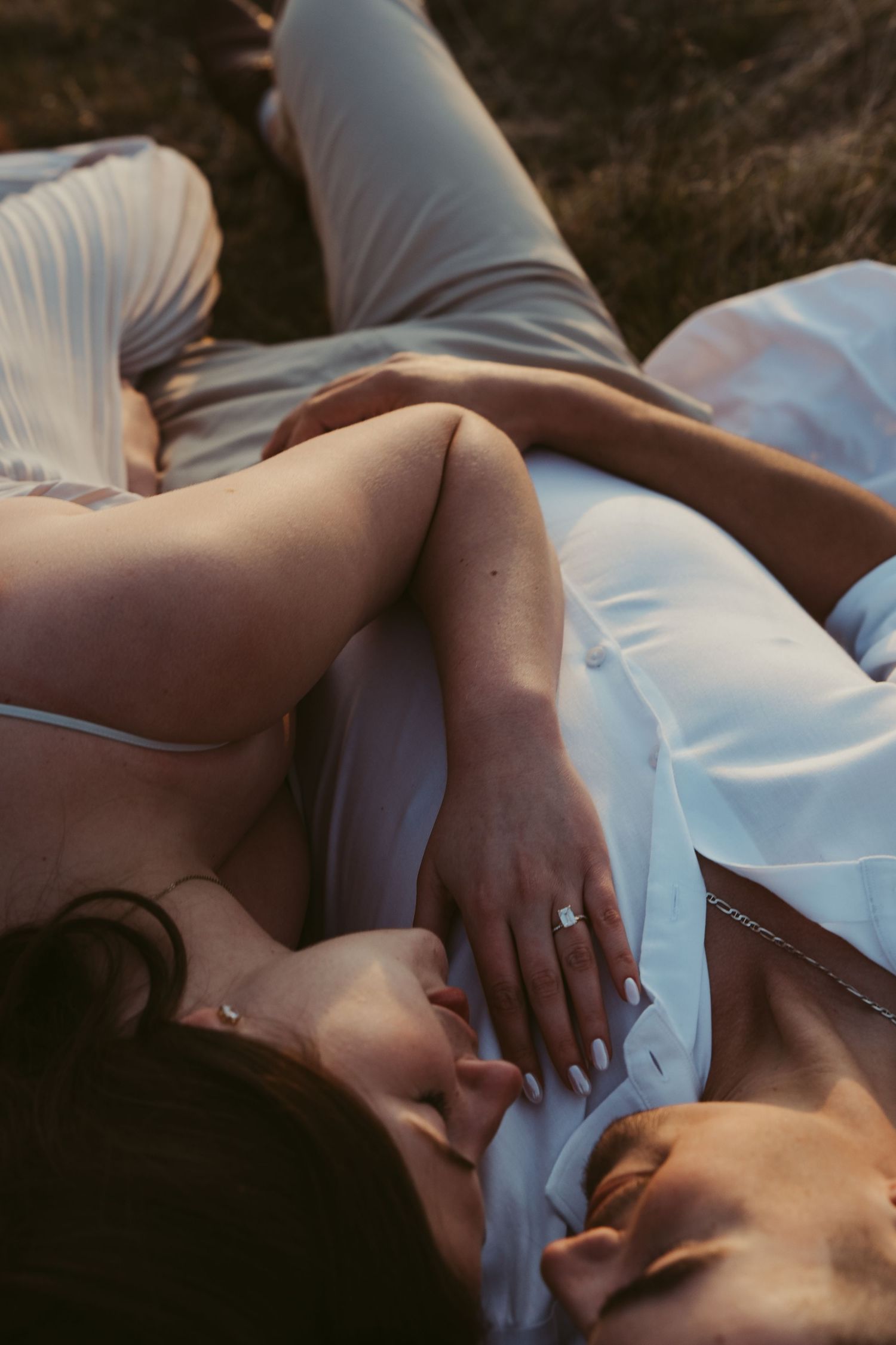 Couple lying close together in white clothing during intimate sunset photoshoot.