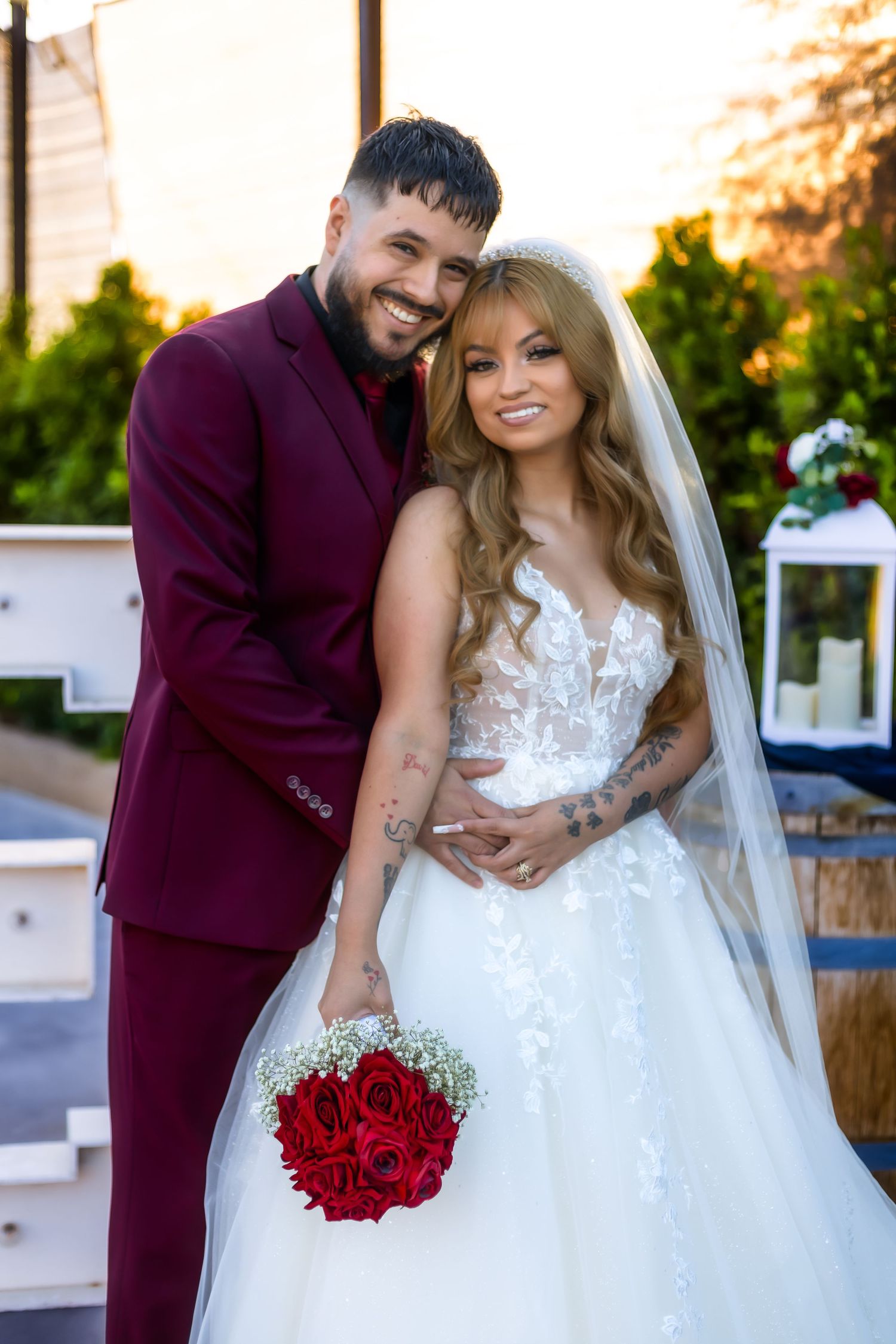 Wedding portrait of couple in burgundy suit and white dress holding red rose bouquet after their wedding in Buckeye Ariziona