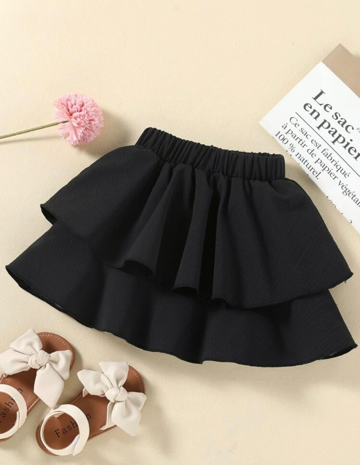 Black layered ruffle mini skirt displayed with white shoes on beige background.