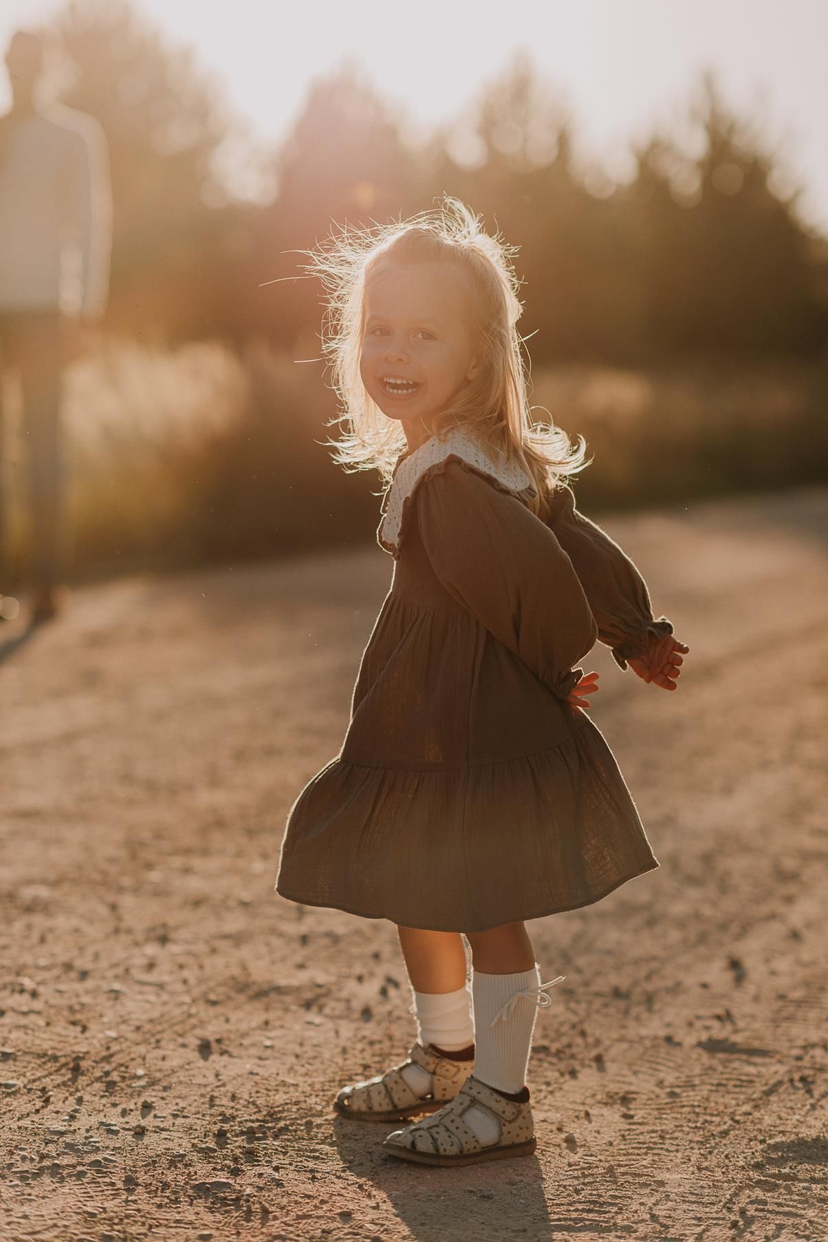 Small child twirls in a dress at sunset on a dirt path.