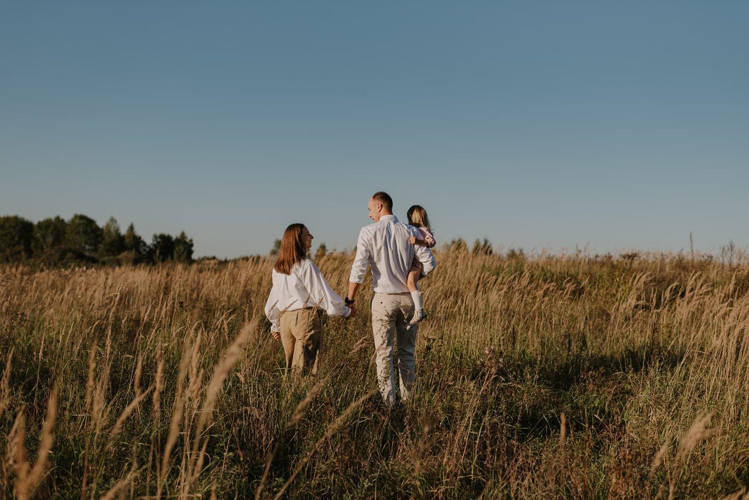 Family silhouettes against blue sky in distance of grassy field.