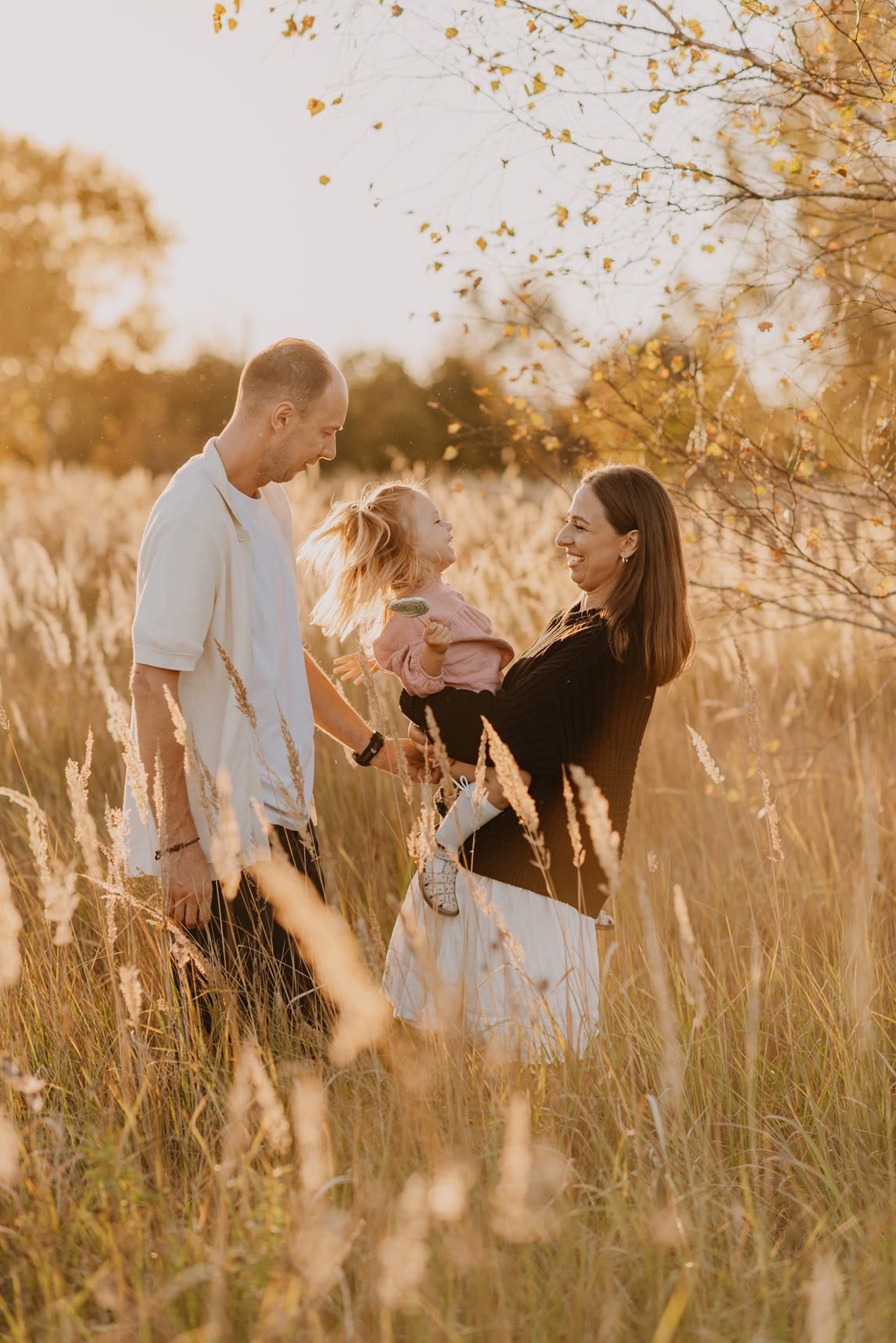 Family embracing in tall grass during sunset photoshoot.